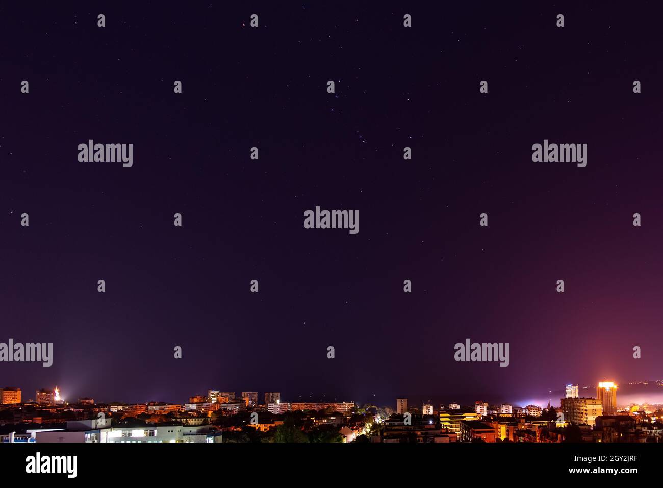 La costellazione Orion splende luminosamente nel cielo scuro sullo skyline illuminato della città a mezzanotte. Cielo stellato chiaro su Varna in autunno. Cielo notturno. Foto Stock