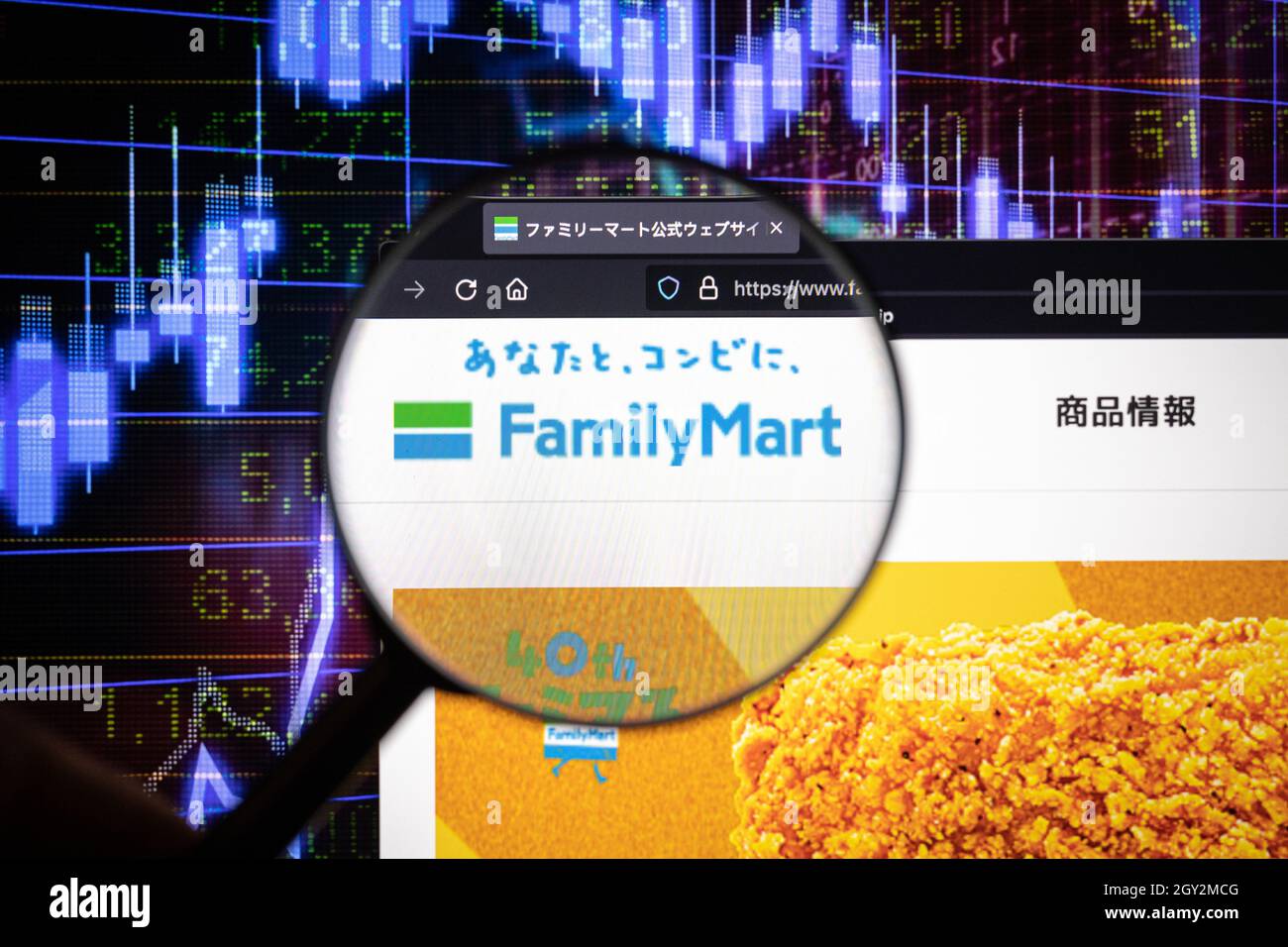 FamilyMart Company logo su un sito web con blurry sviluppi del mercato azionario in background, visto su uno schermo del computer attraverso una lente d'ingrandimento Foto Stock