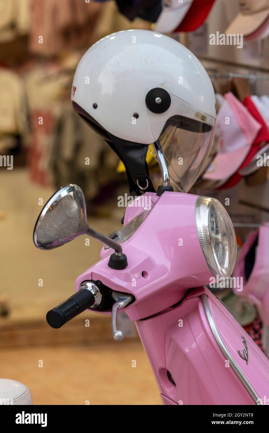 casco in vetroresina bianca sul manubrio di uno scooter a motore rosa sul lato della strada a zante zante grecia. ciclomotore rosa con copricapo. Foto Stock