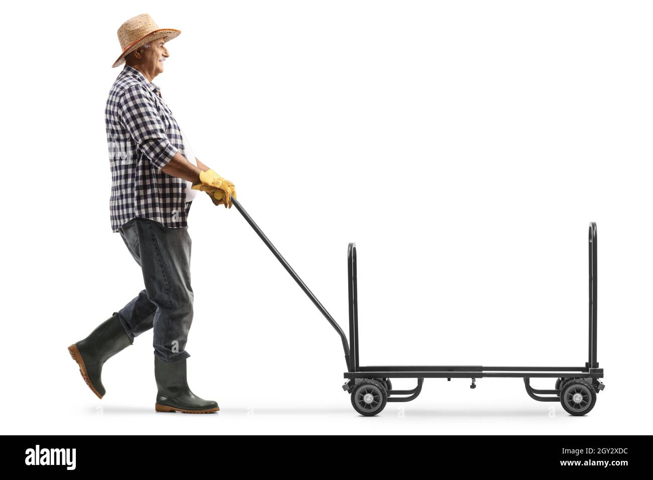 Colpo di profilo a tutta lunghezza di un agricoltore maturo che cammina e spinge un camion a mano vuoto isolato su sfondo bianco Foto Stock