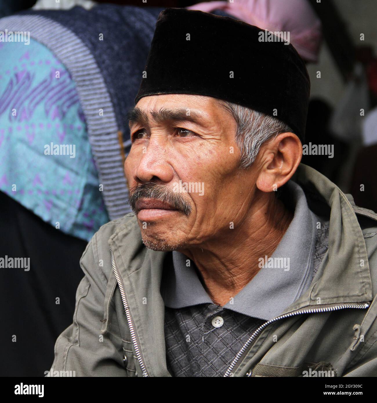 Un vecchio uomo che indossa un cappello di peci musulmano nero mentre fuma una sigaretta in un mercato a Bukittinggi, Sumatra occidentale, Indonesia. Foto Stock