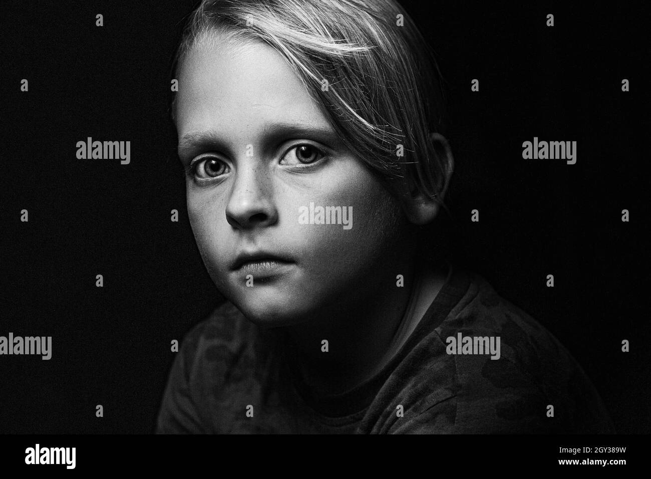 Scatto in scala di grigi di un ragazzo caucasico con grandi occhi profondi che guardano la fotocamera su uno sfondo nero Foto Stock