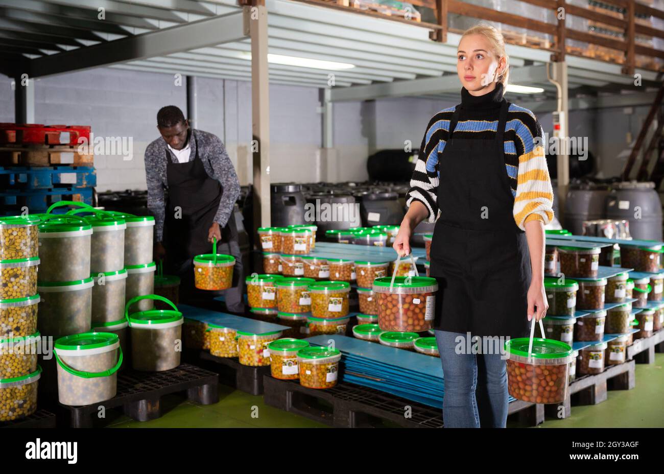Lavoratore di sesso femminile che le scorte di contenitori di plastica e lattine con olive in magazzino Foto Stock