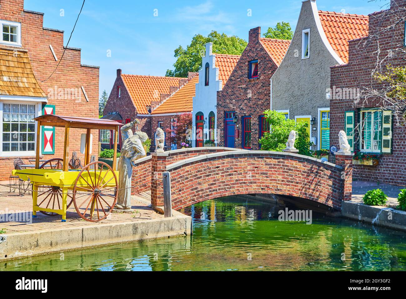 Architettura olandese con cart, statue, canale, e ponte di mattoni accanto ai negozi Foto Stock