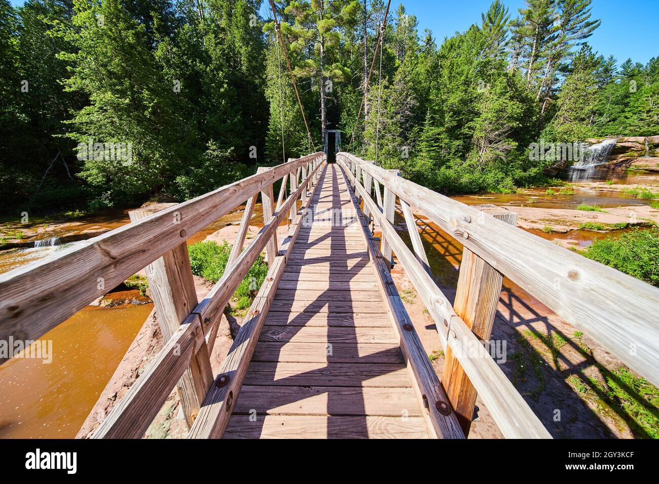Camminando sul ponte sospeso sopra il fiume marrone con la cascata in distanza Foto Stock