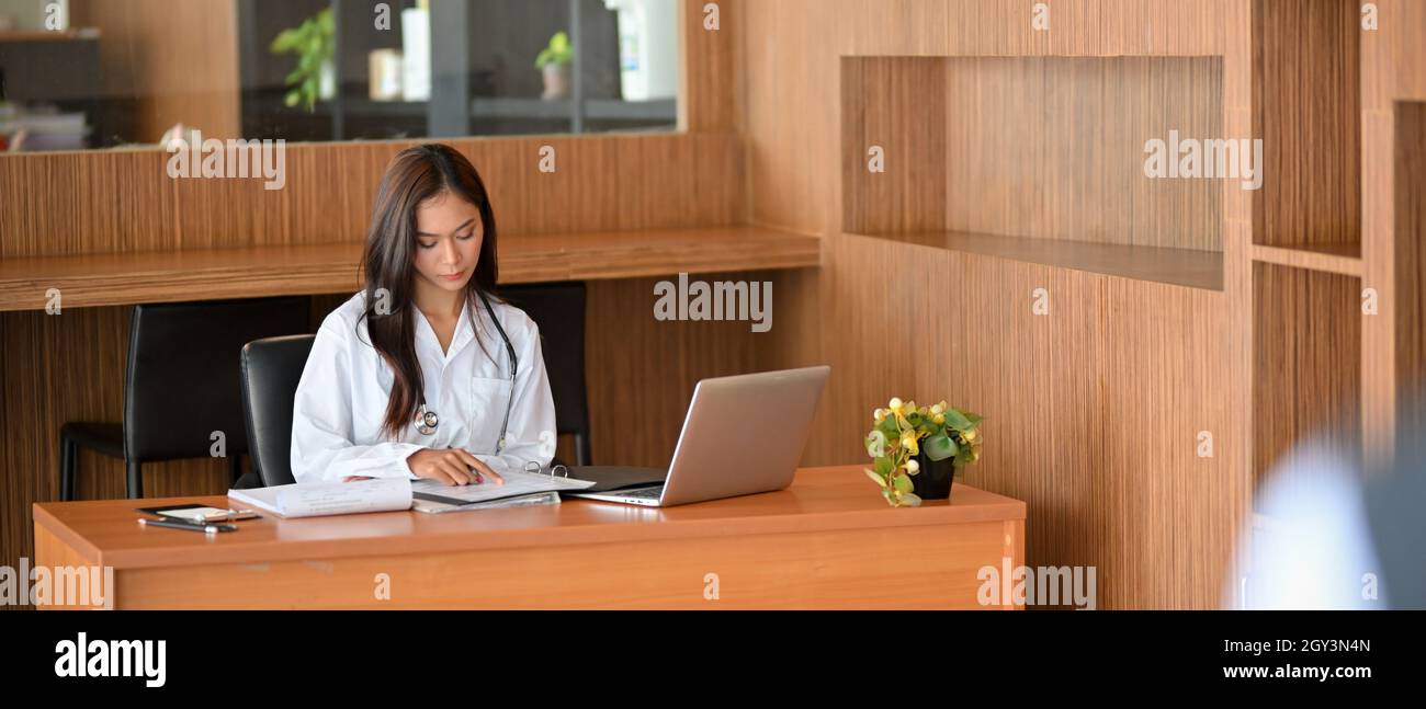 Medico femminile asiatico o dentista che legge un documento di ricerca medica o passato storia medica documenti in ospedale ufficio. Medico ufficio concetto di lavoro Foto Stock