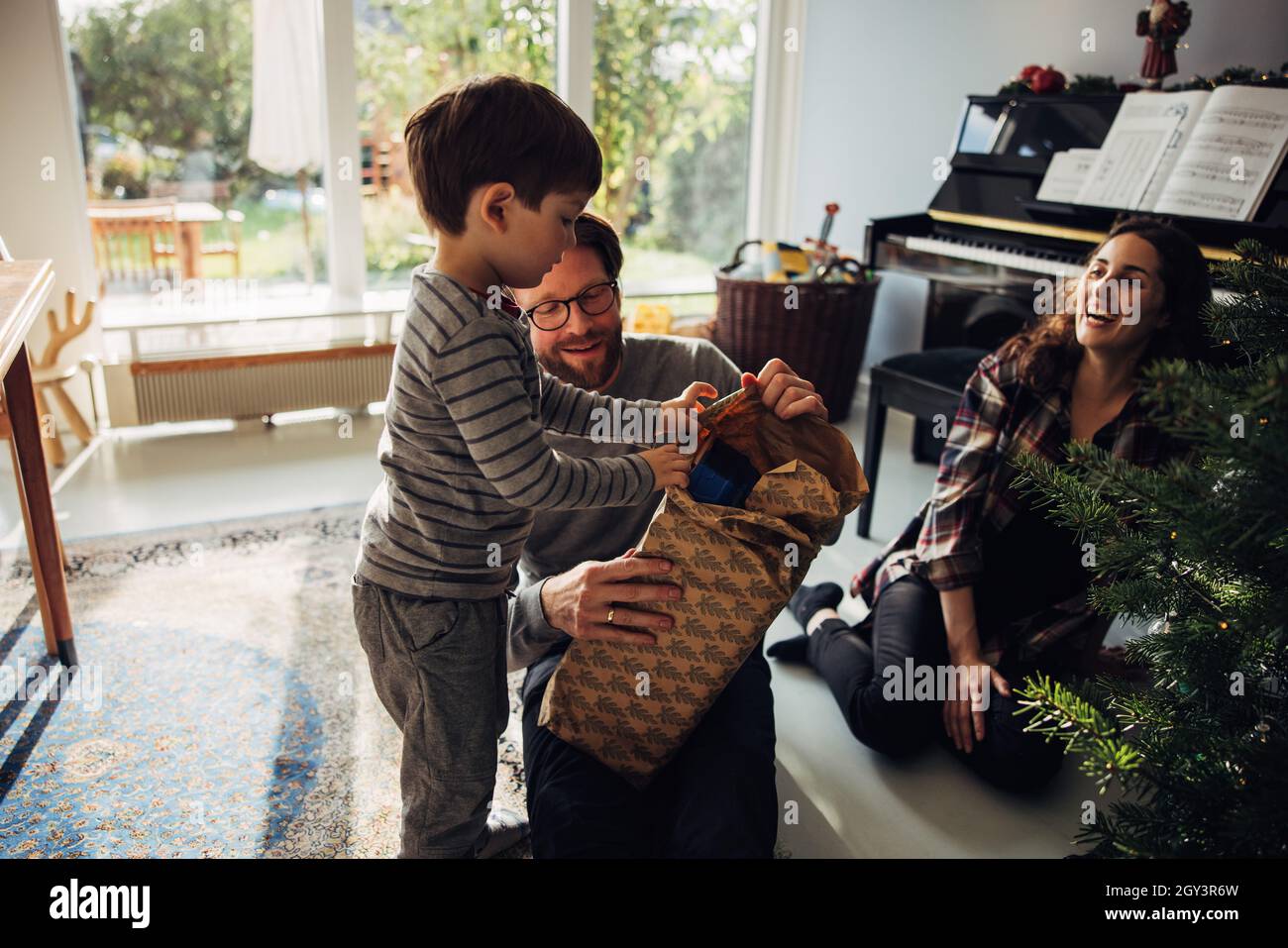 Famiglia che apre i regali di Natale insieme a casa. Padre che aiuta il figlio ad aprire i suoi regali mentre siede da albero di Natale a casa. Foto Stock