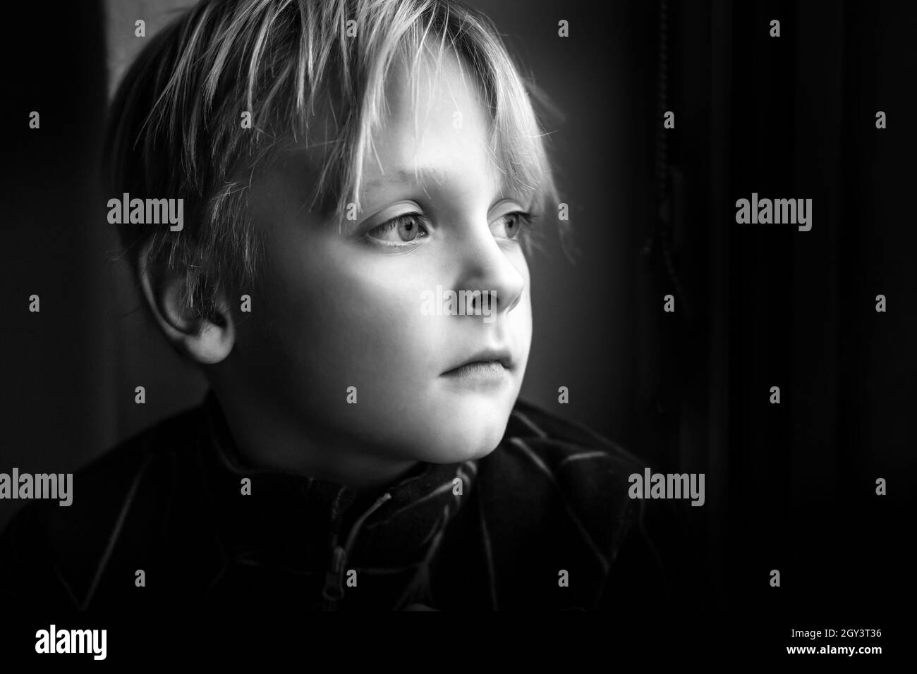 Scatto in scala di grigi di un ragazzo caucasico con grandi occhi profondi su sfondo nero Foto Stock