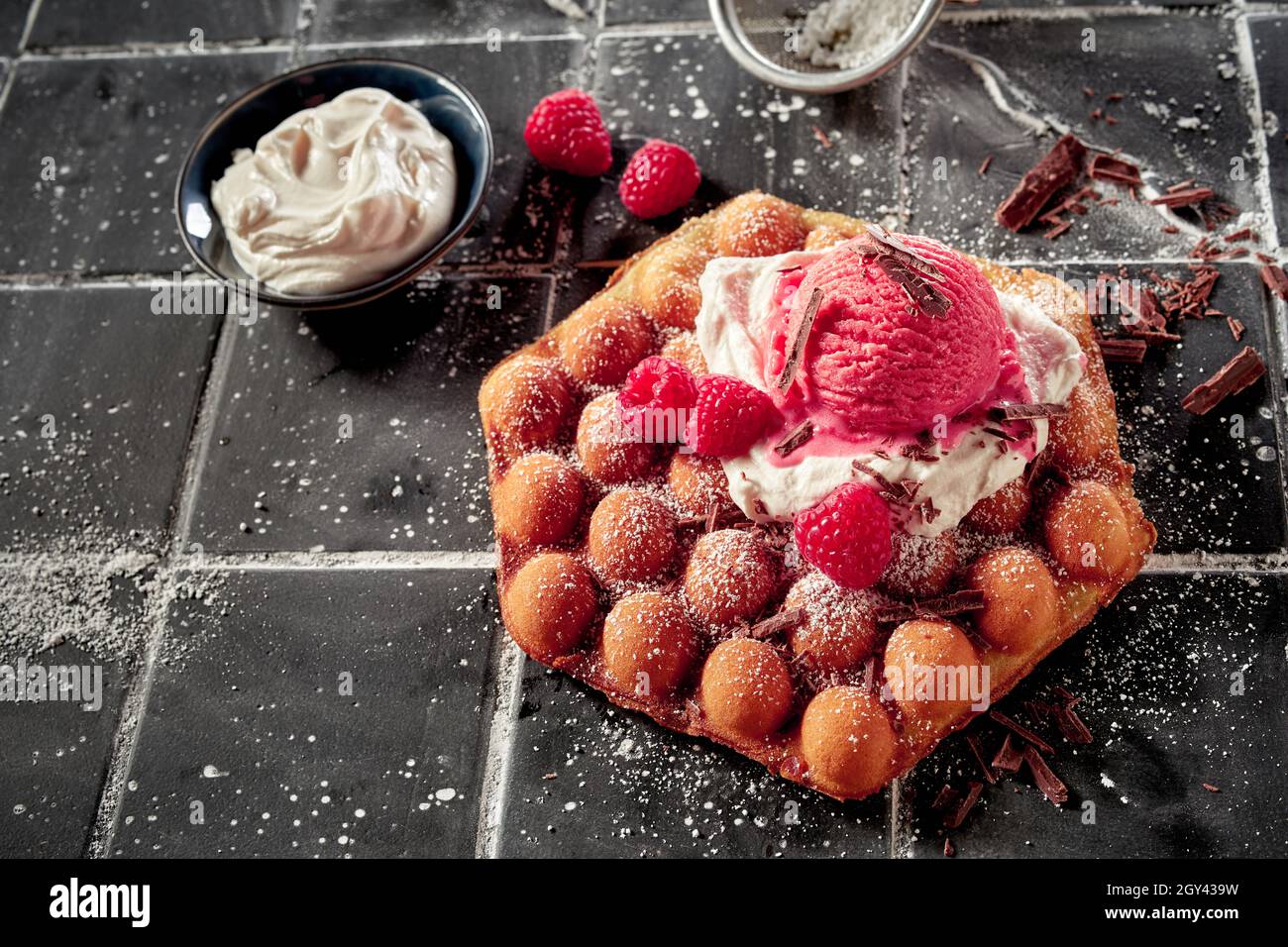 Delizioso waffle a forma di bolla di lampone con una bambola di panna montata e gelato fruttato di stagione alla bacche, condito con fiocchi di cioccolato e cosparso di ic Foto Stock