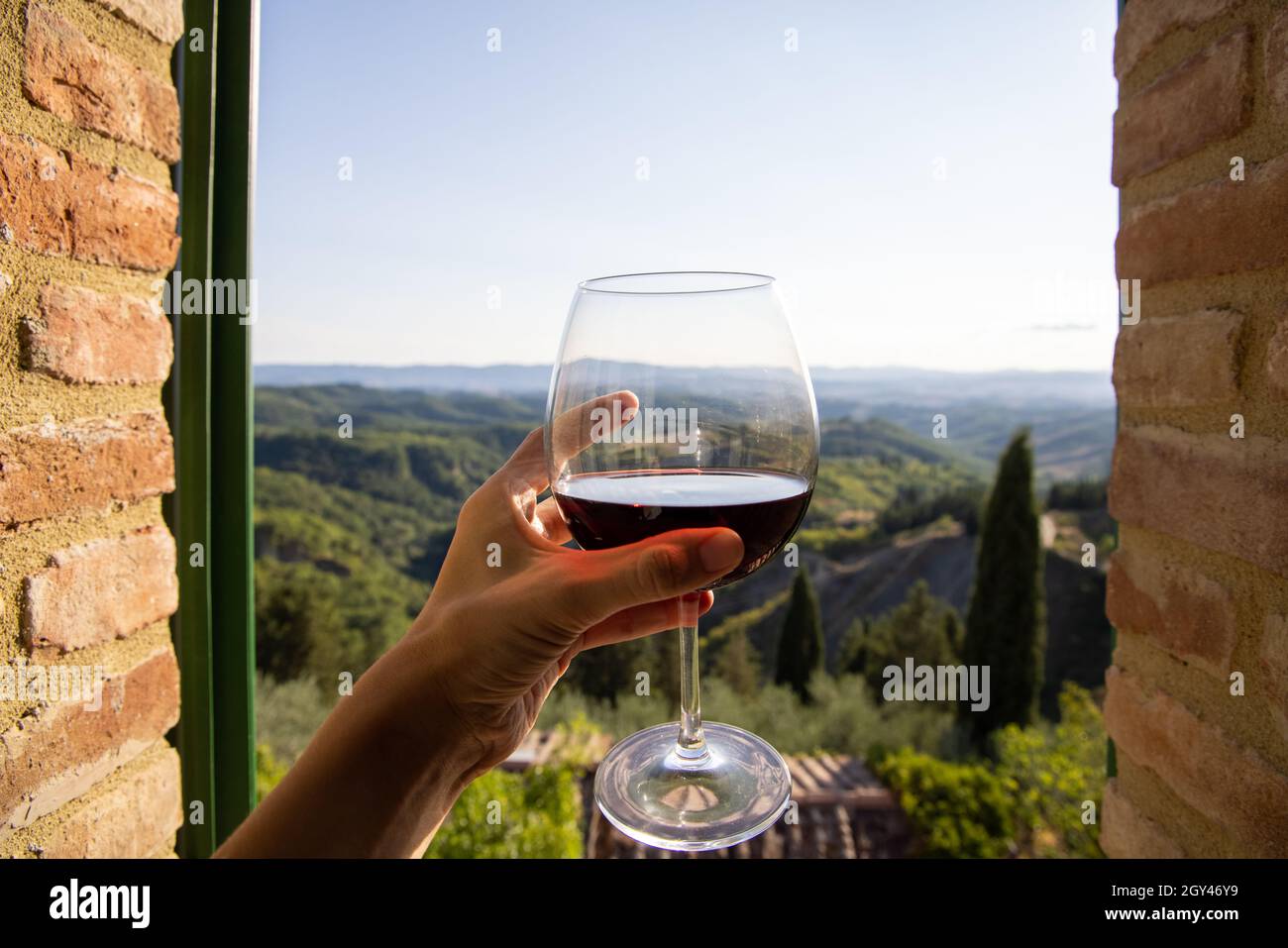 Donna che tiene un bicchiere di vino rosso con un bellissimo paesaggio d' Italia sullo sfondo in una giornata di sole. Vista dalla finestra Foto  stock - Alamy