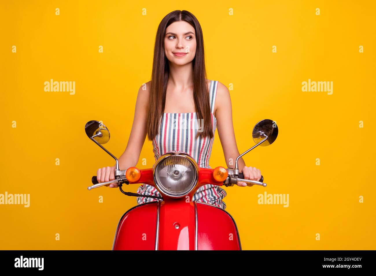 Foto ritratto giovane donna che guida in bicicletta in abito a righe guardando spazio vuoto isolato colore giallo brillante sfondo Foto Stock