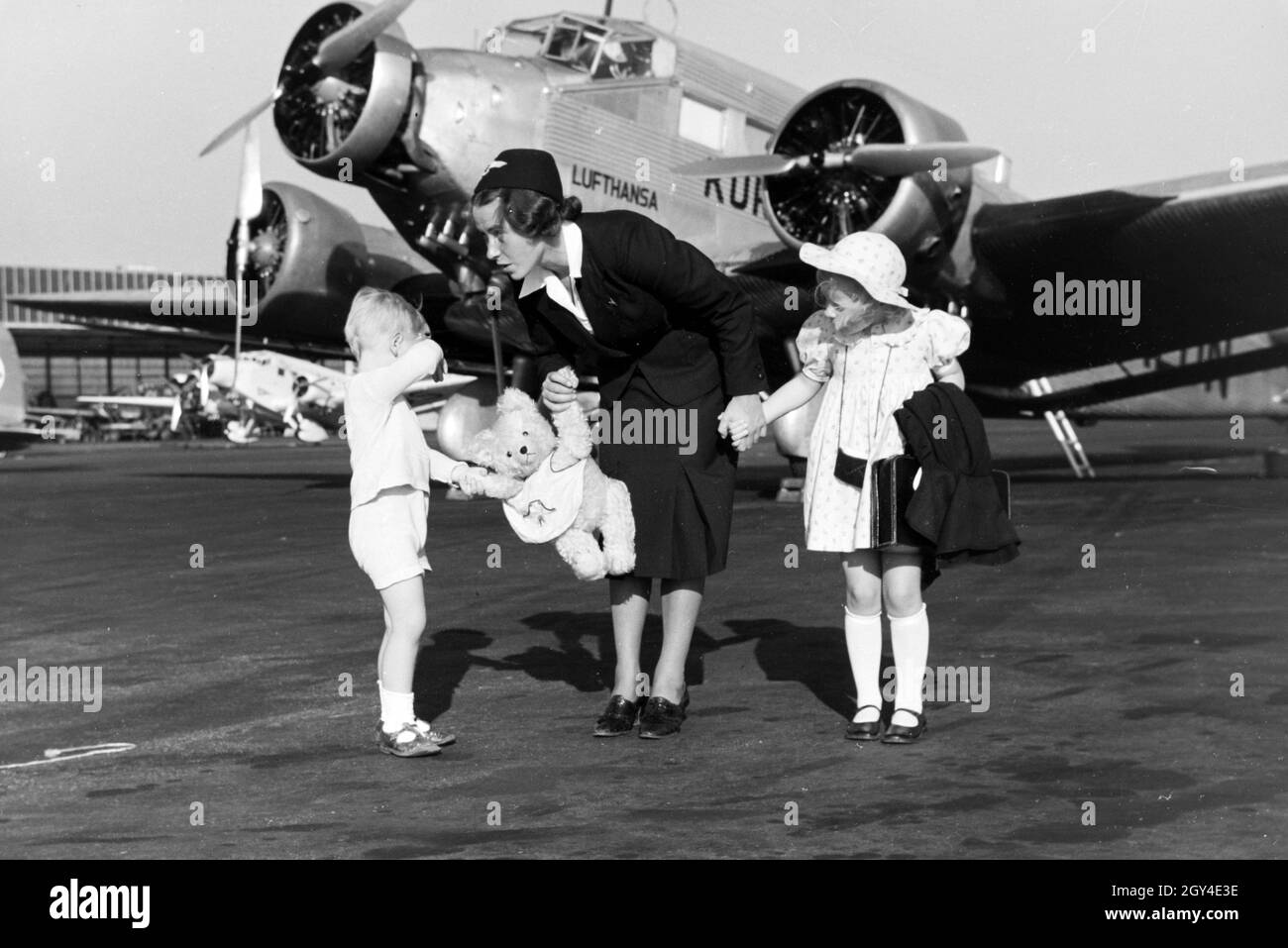 Eine hostess"führt zwei Kinder über das Flugfeld zum Flugzeug, Deutschland 1930er Jahre. Hostess che portano due bambini oltre l'aviosuperficie al piano, Germania 1930s. Foto Stock