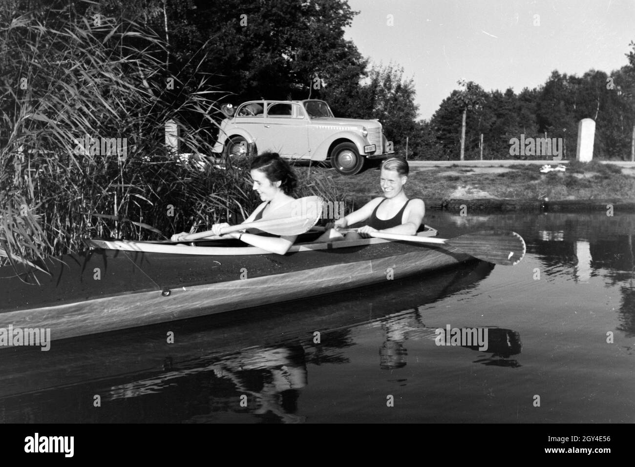 Junges Paar paddelt im Boot in Nähe des Ufers auf einem vedere, Deutschland 1930er jahre. Coppia giovane paddling in una barca sul lago vicino al fiume, Germania 1930s. Foto Stock