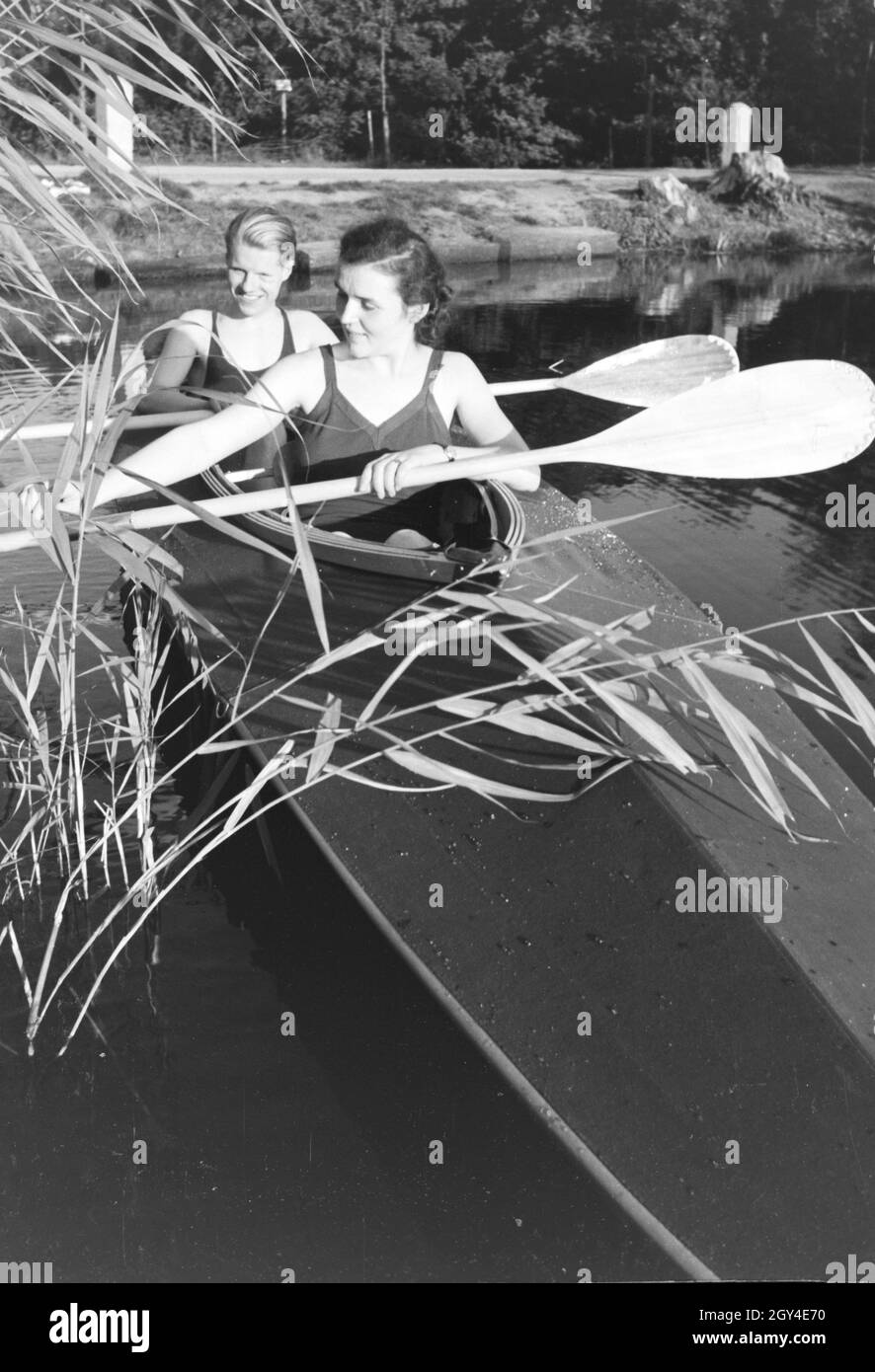 Junges Paar paddelt im Boot in Nähe des Ufers auf einem vedere, Deutschland 1930er Jahre. Coppia giovane paddling in una barca sul lago vicino al fiume, Germania 1930s. Foto Stock