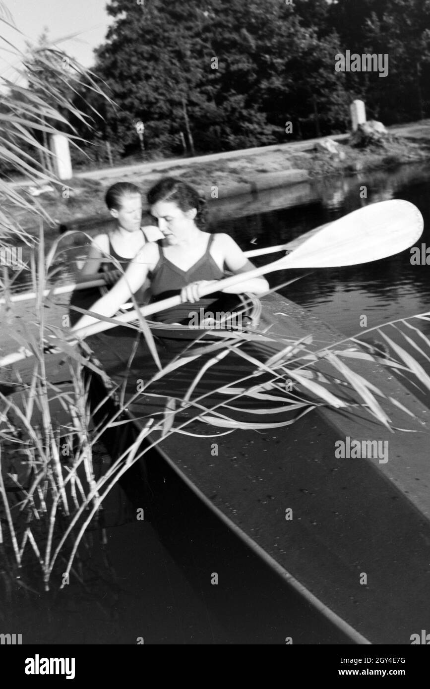 Junges Paar paddelt im Boot in Nähe des Ufers auf einem vedere, Deutschland 1930er Jahre. Coppia giovane paddling in una barca sul lago vicino al fiume, Germania 1930s. Foto Stock