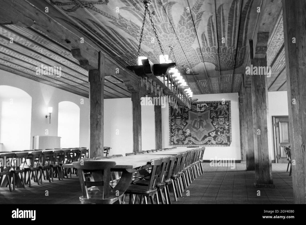 Ansicht eines Saals mit langer Tafel, Kronleuchter und Dekorationen / Reichsadler / Adler Motiv auf der Holzdecke und Teppich / Bild an der Wand, Deutschland 1930er Jahre. Vista di una sala con un lungo tavolo, lampadario e decorazioni / Imperial Eagle / eagle movente sul soffitto in legno e tappezzeria / quadro appeso alla parete, Germania 1930s. Foto Stock