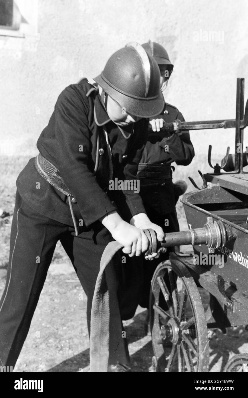 Zwei uniformierte Jungen von der Kinderfeuerwehr installieren bei einer Feuerwehrübung den Wasserschlauch, Deutschland 1930er Jahre. Due ragazzi in uniforme della junior sono i vigili del fuoco di installare il tubo flessibile di acqua durante un vigile del fuoco di formazione, Germania 1930s. Foto Stock