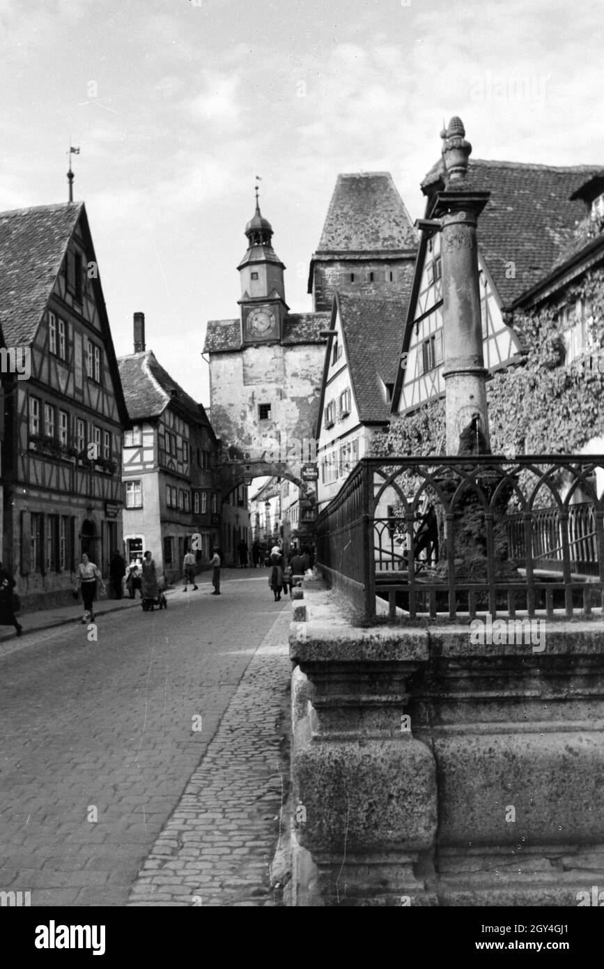 Am von Fußgängern belebten Platz vor dem Röderbogen a Rothenburg ob der Tauber befindet sich einer der vielen Springbrunnen der Stadt, Deutschland 1930er Jahre. Sulla piazza trafficata di fronte al Röder arch a Rothenburg ob der Tauber pedoni possono visitare una delle tante fontane della città, Germania 1930s. Foto Stock