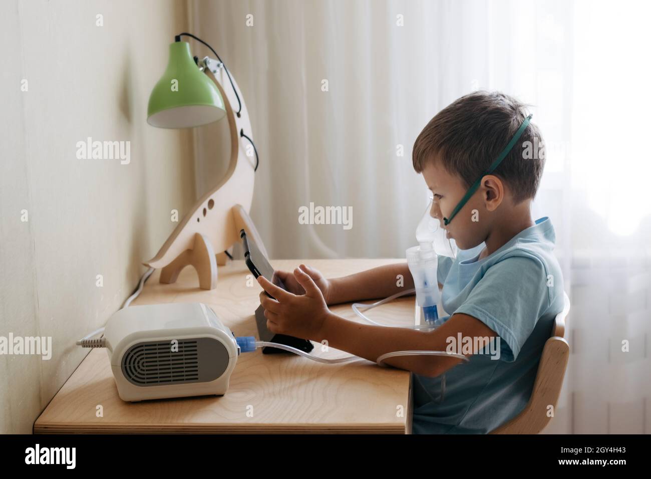 Bambini che siettono al tavolo e guardano il cartone animato sulla compressa durante l'inalazione con il nebulizzatore. Trattamento a casa. Il concetto di salute Foto Stock