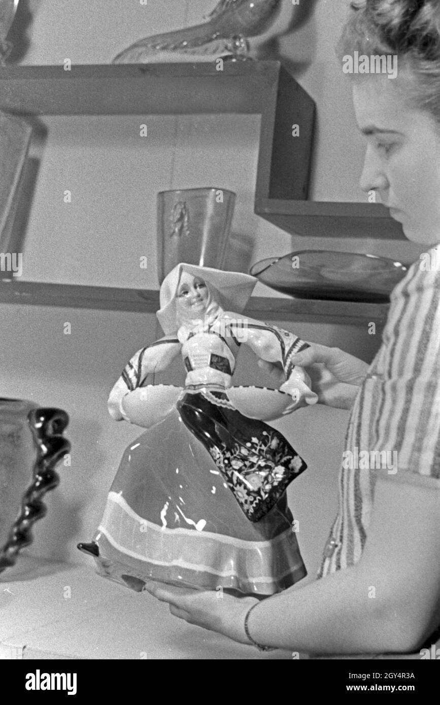 Die Angestellte auf einem Messestand für Porzellan und Keramik mit einer Porzellanfigur auf der Messe Leipzig, Deutschland 1940er Jahre. Una femmina di membro dello staff in uno stand per porcellana e ceramica con una statuetta in Leipzig trade show, Germania 1940s. Foto Stock