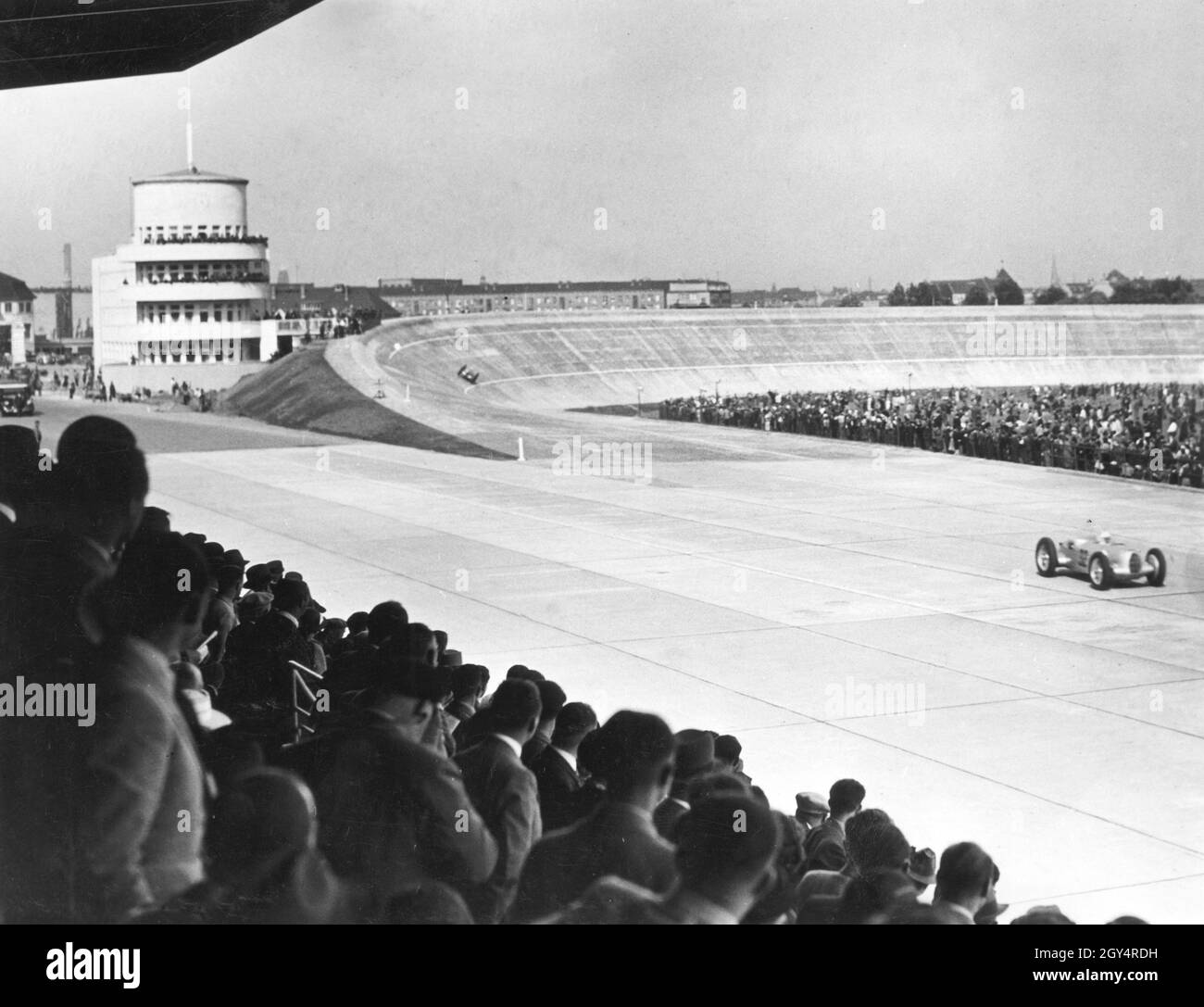 Il 28 maggio 1937 si è svolta a Berlino una gara automobilistica sull'Avus. Qui un pilota (probabilmente in una Mercedes-Benz W 25) passa la nuova costruzione e il tribuna completo dopo aver lasciato la curva nord ricostruita. Sulla sinistra si trova la torre del giudice finale. [traduzione automatizzata] Foto Stock