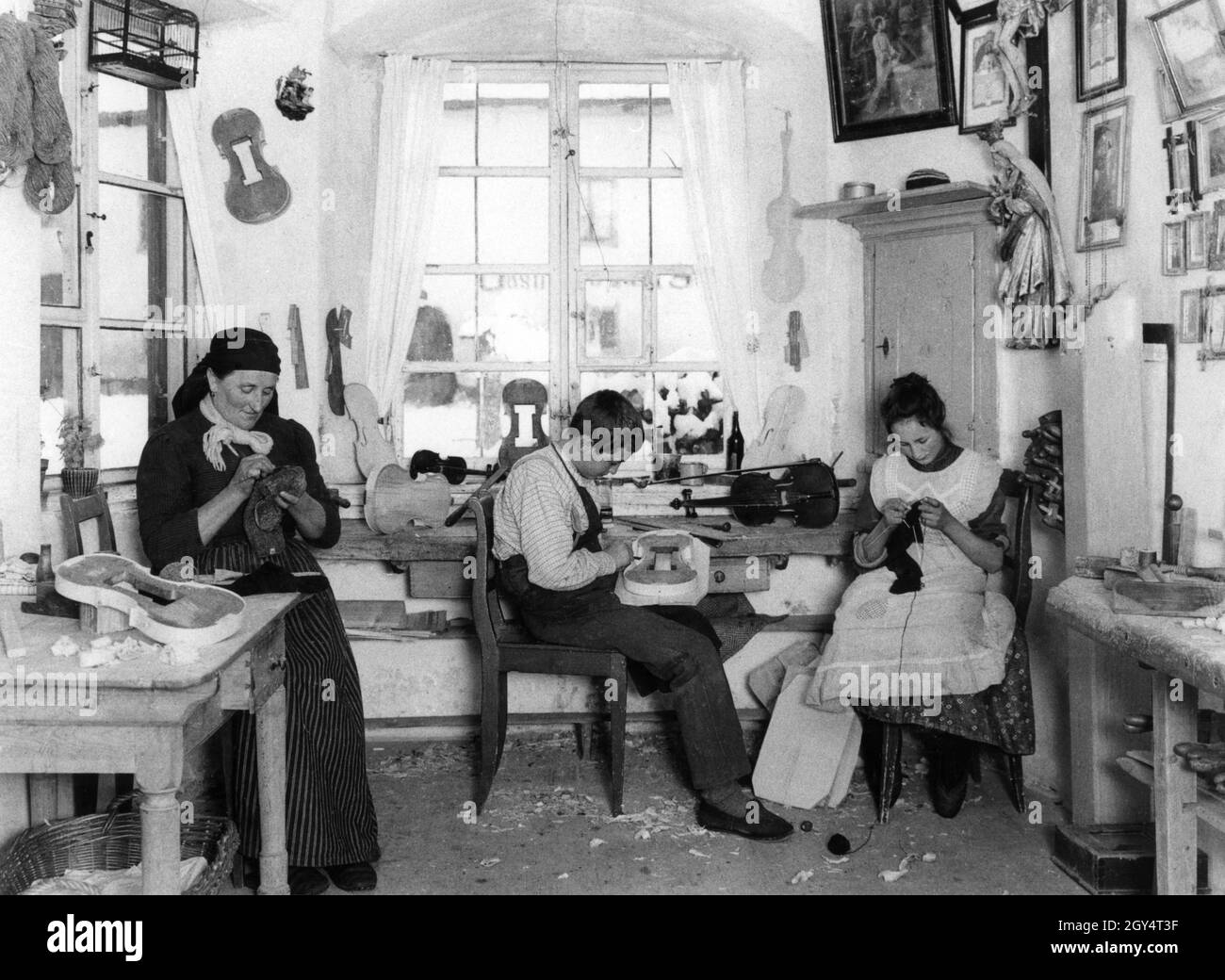 Questa famiglia produce violini nel loro laboratorio a Mittenwald nell'inverno del 1908. I bambini devono anche aiutare con il lavoro, con il ragazzo che forma un violino e la ragazza maglia. [traduzione automatizzata] Foto Stock