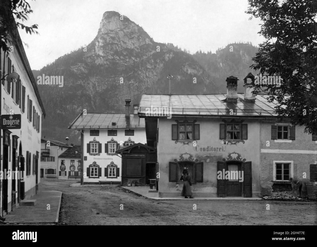 'Nel 1909, i seguenti negozi si trovavano nella Dorfstraße di Oberammergau: La 'Drogerie Ammergau' (a sinistra), un negozio di scarpe e un negozio di sculture (al centro) e una ''Conditorei' (a destra). Sullo sfondo c'è il Kofel. [traduzione automatizzata]' Foto Stock