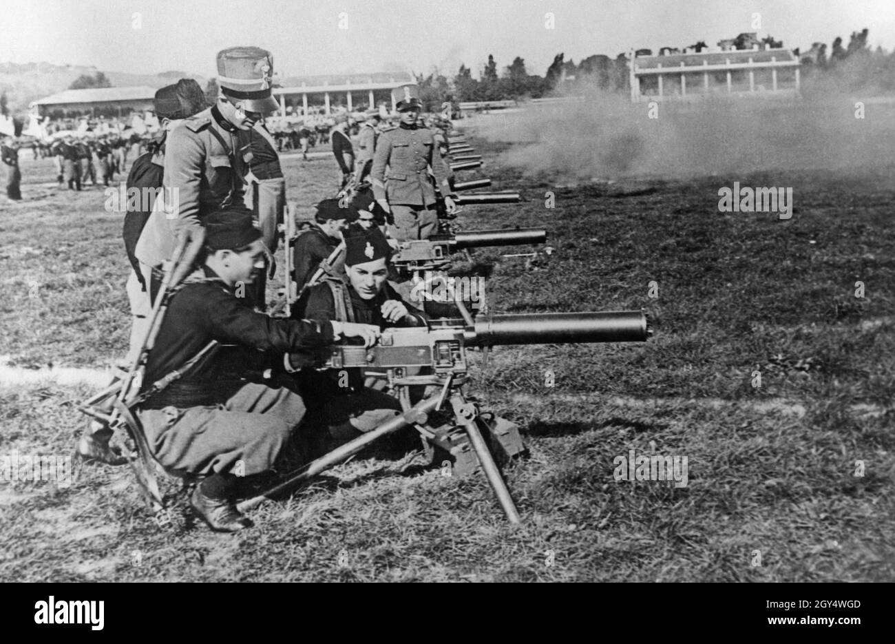 In un campo di allenamento vicino a Roma, i membri dell'organizzazione giovanile fascista Opera Nazionale Balilla praticano il funzionamento di una mitragliatrice. Due giovani alla volta gestiscono uno dei fucili sotto la supervisione di un ufficiale dell'esercito italiano. Il Duca di Spoleto, Principe Aimone di Aosta, visitò l'esercizio. [traduzione automatizzata] Foto Stock