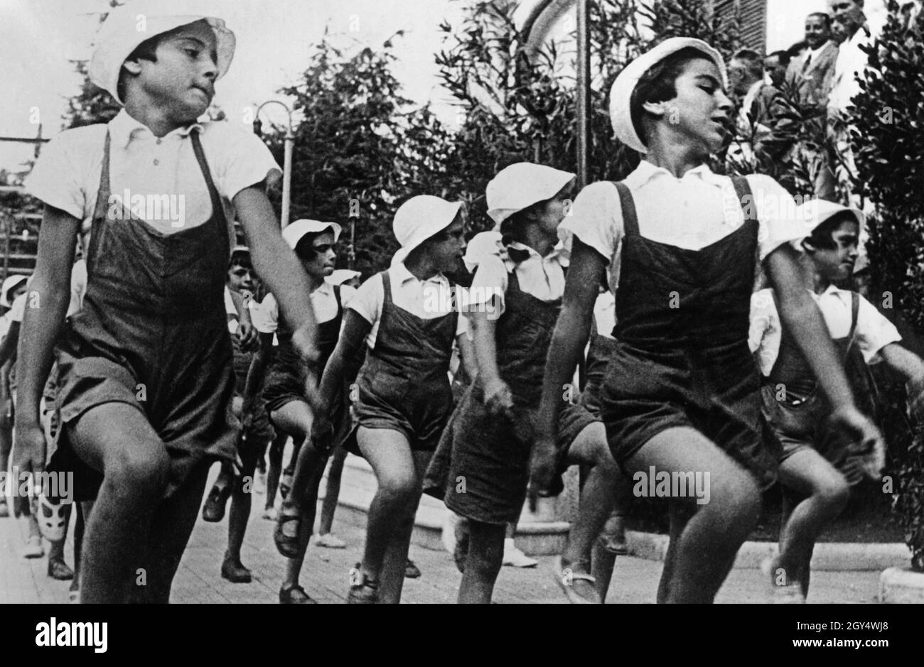 'Queste ragazze marciano nel 1937 in un unico file, i loro occhi si girarono di lato, guardato da alcuni adulti (a destra). Le ragazze appartengono alle ''piccole italiane'', le ragazze di età compresa tra 8 e 14 anni nell'ambito dell'organizzazione giovanile fascista italiana Opera Nazionale Balilla. [traduzione automatizzata]' Foto Stock