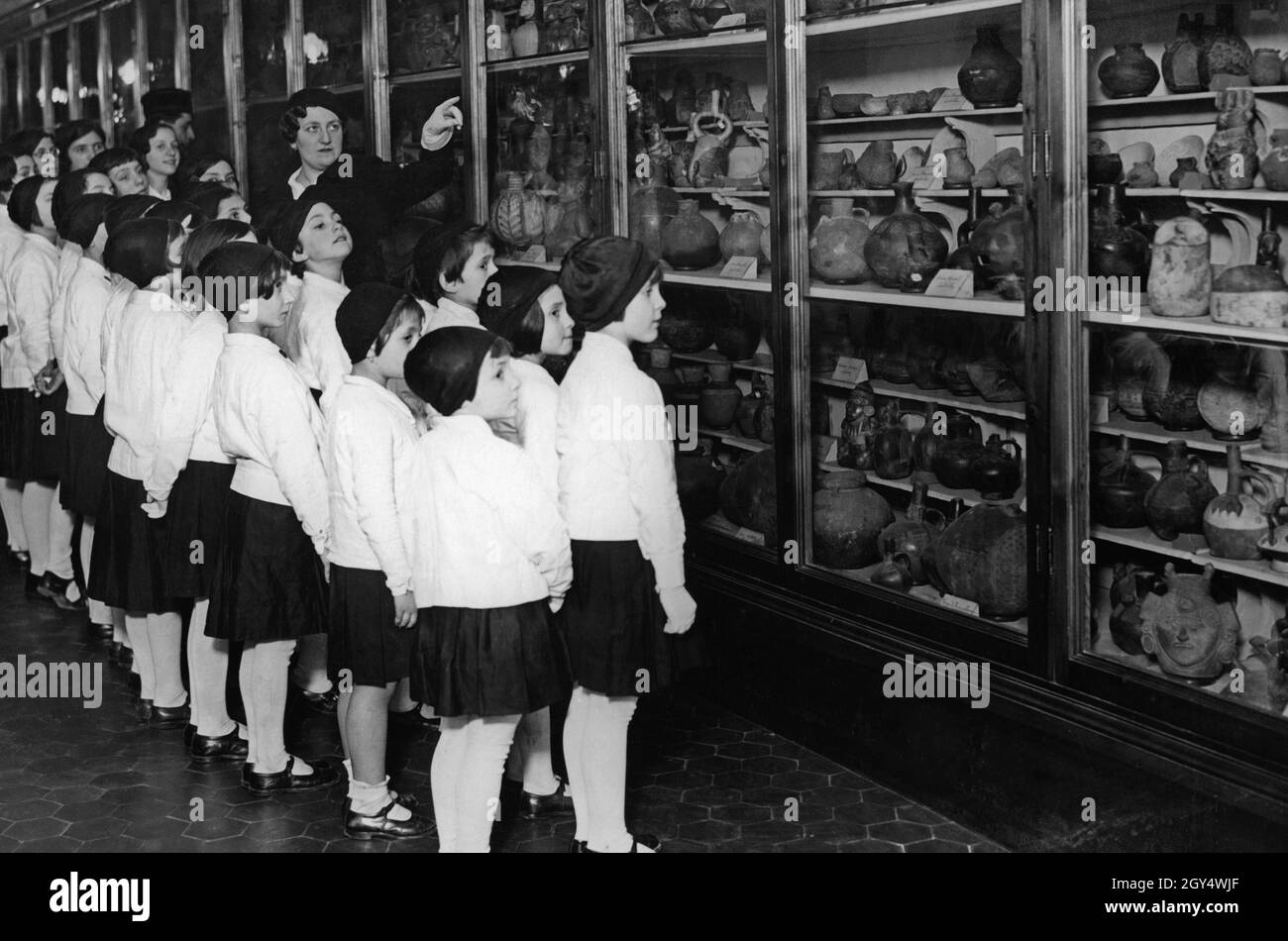 Una classe femminile italiana visita un museo nel 1934. L'insegnante indica gli oggetti visualizzati negli armadietti e li spiega agli studenti. Negli armadi sono vasi antichi, vasi e sculture in argilla o legno. [traduzione automatizzata] Foto Stock