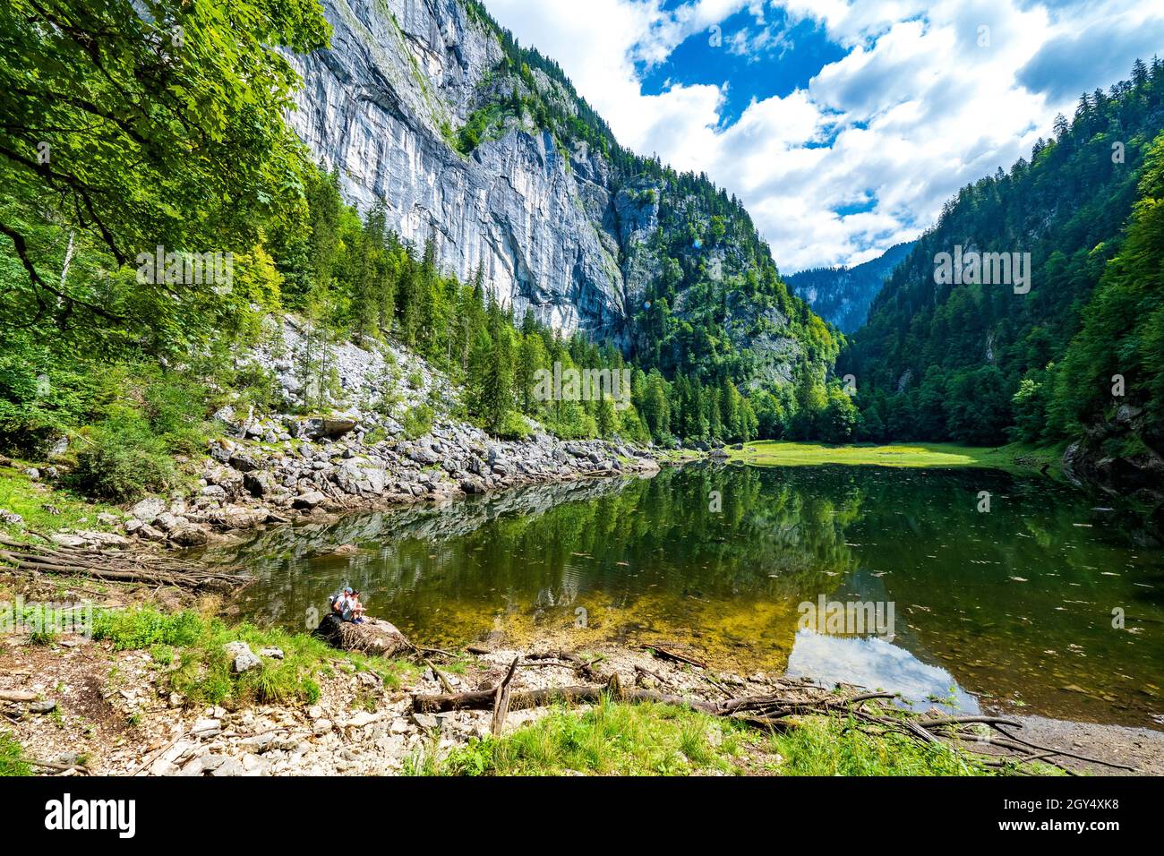 Escursionisti seduti su una roccia al lago di Kammersee, Ausseer Land, Stiria, Austria, che è racchiusa da montagne e una foresta primordiale Foto Stock