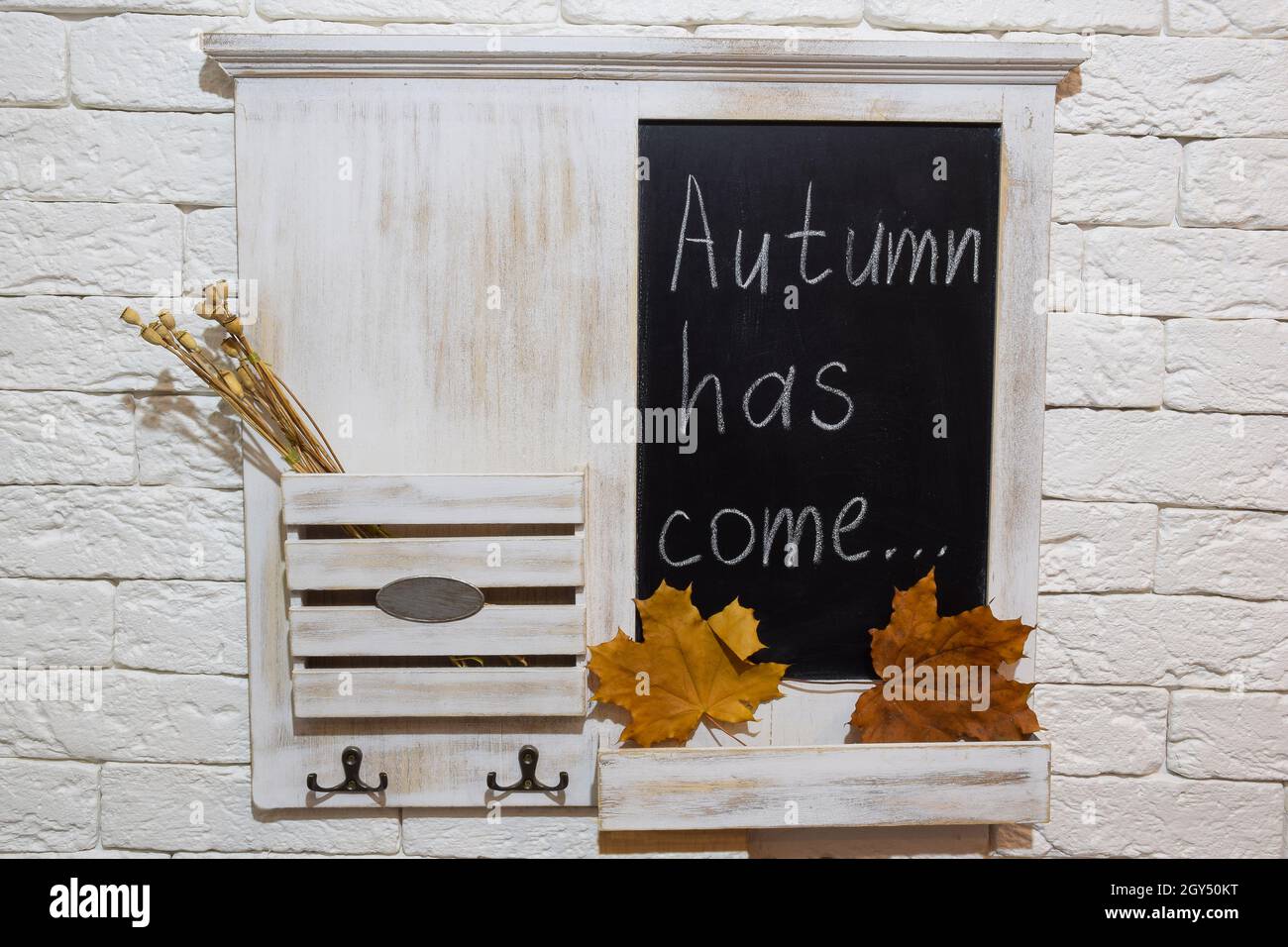 Ripiano decorativo sul muro nel corridoio per posta e chiavi con l'iscrizione AUTUNNALE HA KOME. Ha foglie di acero giallo autunno, piante appassite Foto Stock