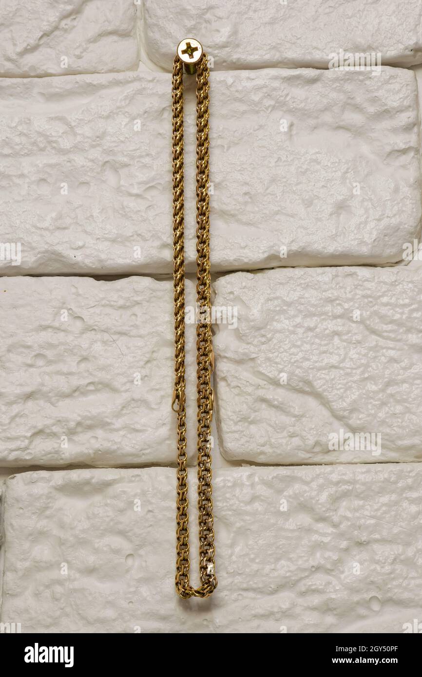 Catena in oro appesa a una vite su una parete in mattoni decorativi di colore chiaro al centro del telaio Foto Stock