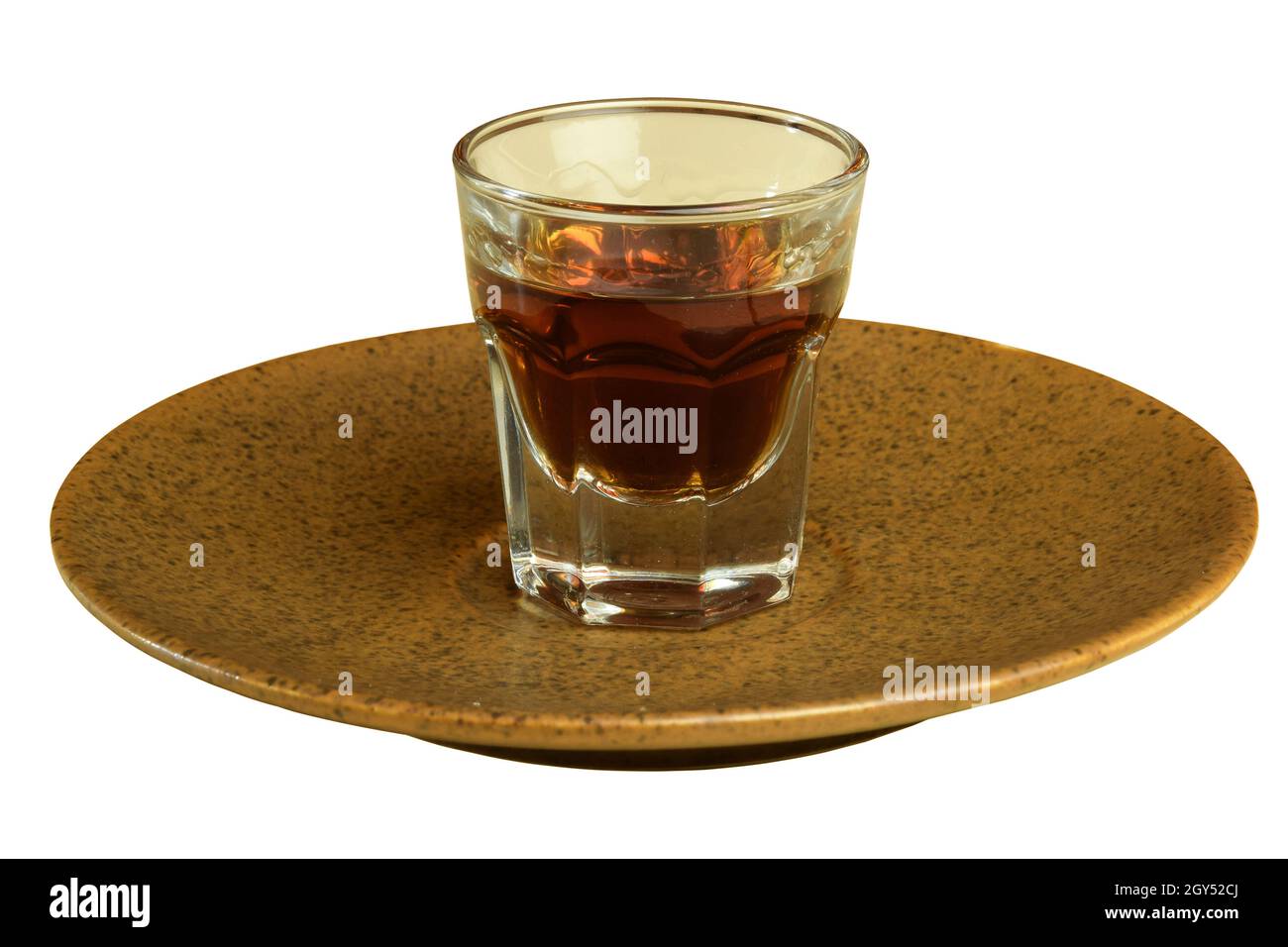 C'è un bicchiere di cognac su un piattino di ceramica marrone su sfondo bianco. Primo piano fotografato. Foto Stock