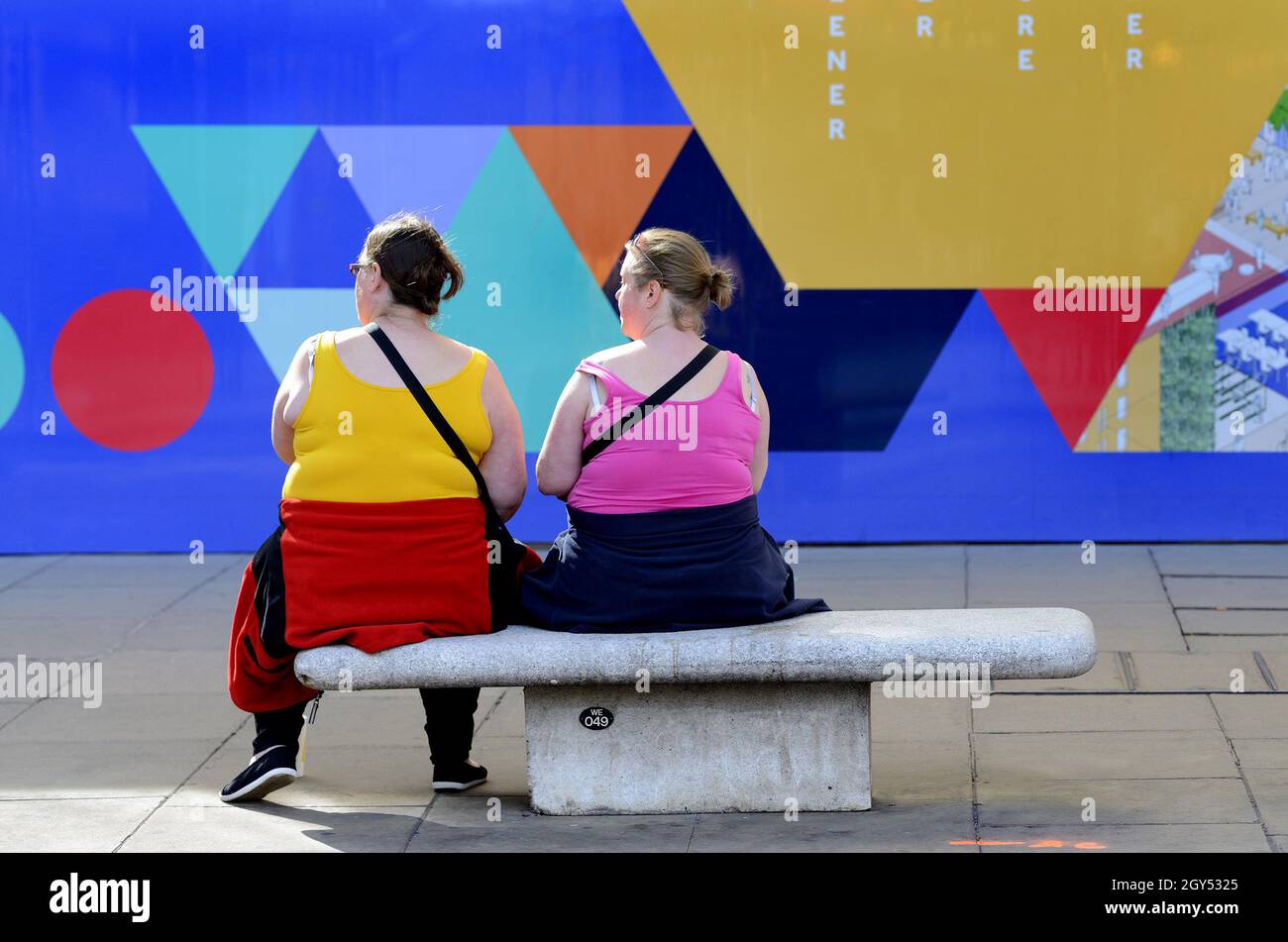 Londra, Inghilterra, Regno Unito. Due donne colorate sedute di fronte a una parete colorata a Oxford Street in una giornata di sole nel mese di ottobre [no model release] Foto Stock
