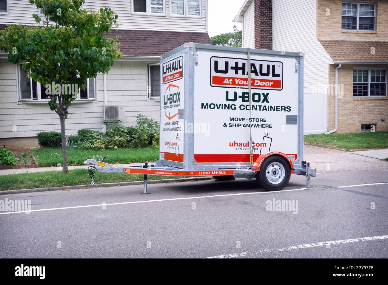 Un U-Haul U-Box che sposta il contenitore su un rimorchio fuori delle piccole case private a Queens, New York City. Foto Stock