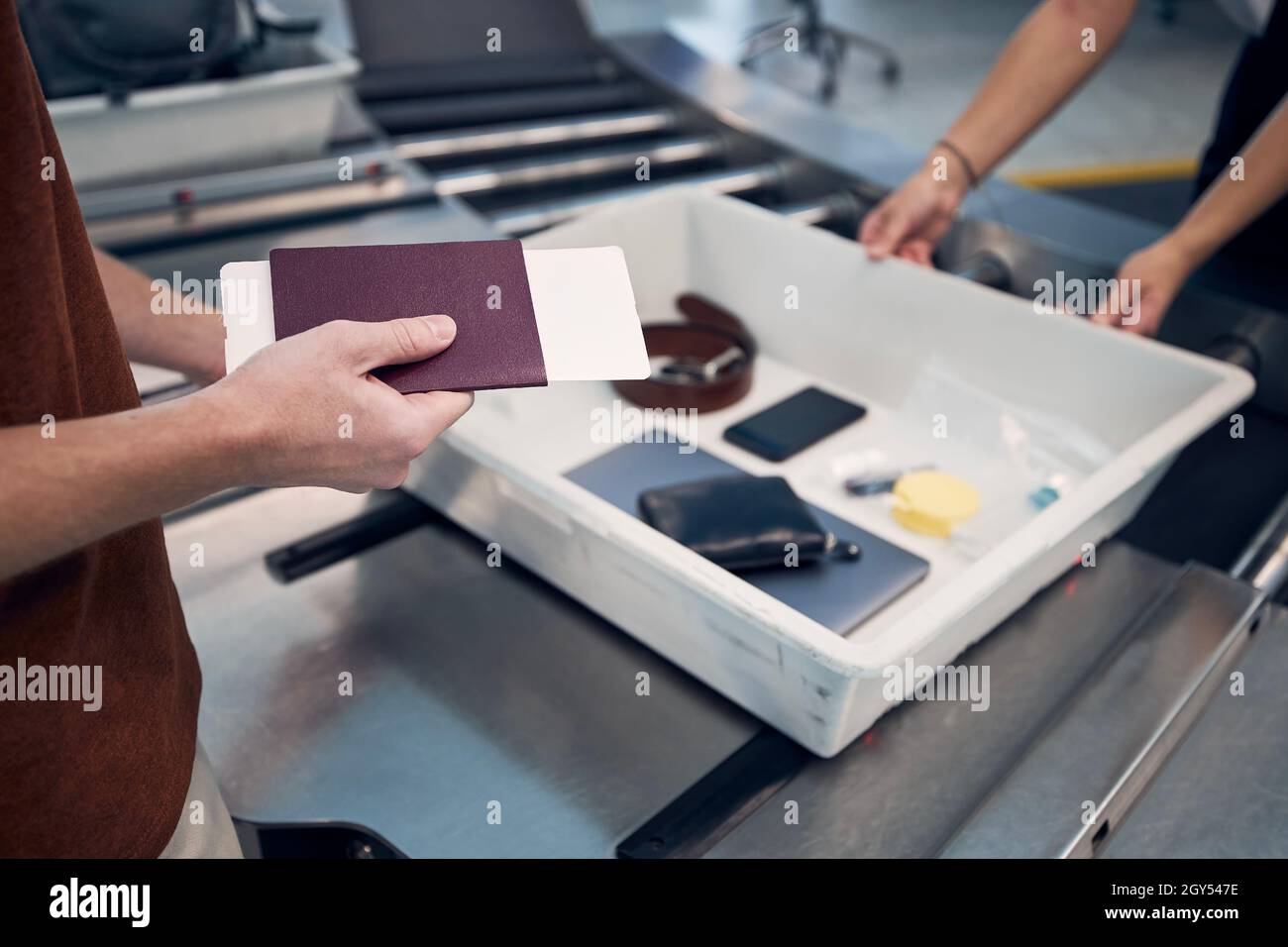 Il passeggero che detiene il passaporto contro oggetti personali, liquidi e computer portatile in contenitore al controllo di sicurezza dell'aeroporto. Foto Stock