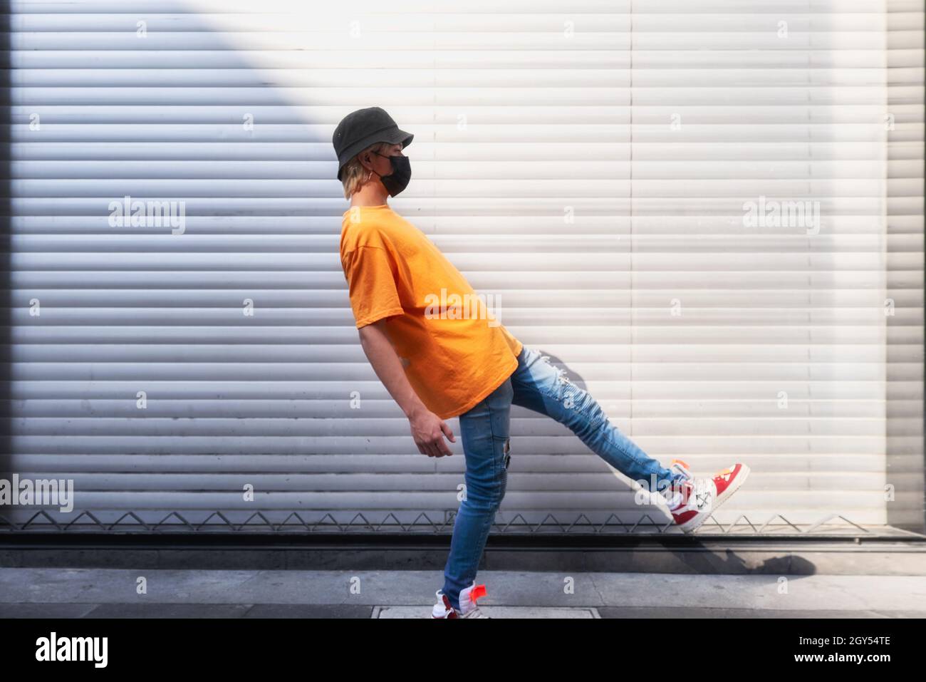 Primo piano di un modello ragazzo che indossa una maschera e un cappello, arancione t.shirt in pubblico, moda modeling Foto Stock