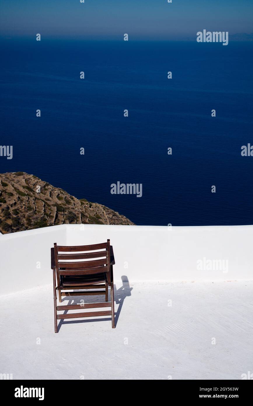 Isola di Sikinos Grecia sedia solitaria su una terrazza con vista spettacolare dall'alto sopra il mare all'orizzonte verticale scatto con spazio copia Foto Stock