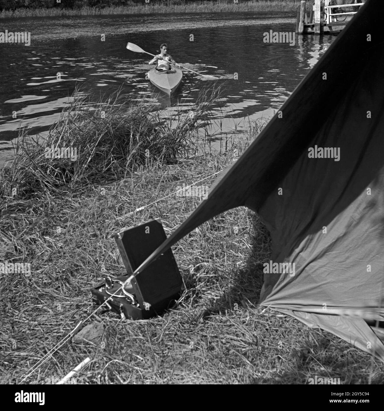Ein Mann paddelt in einem Klepper Faltboot auf das Ufer zu, wo ein Klepper Zelt aufgebaut Ist Deutschland 1930er Jahre. Un uomo sguazzare nella sua piegatura Klepper barca alla riva di un laghetto, dove una tenda Klepper è costruito, Germania 1930s. Foto Stock