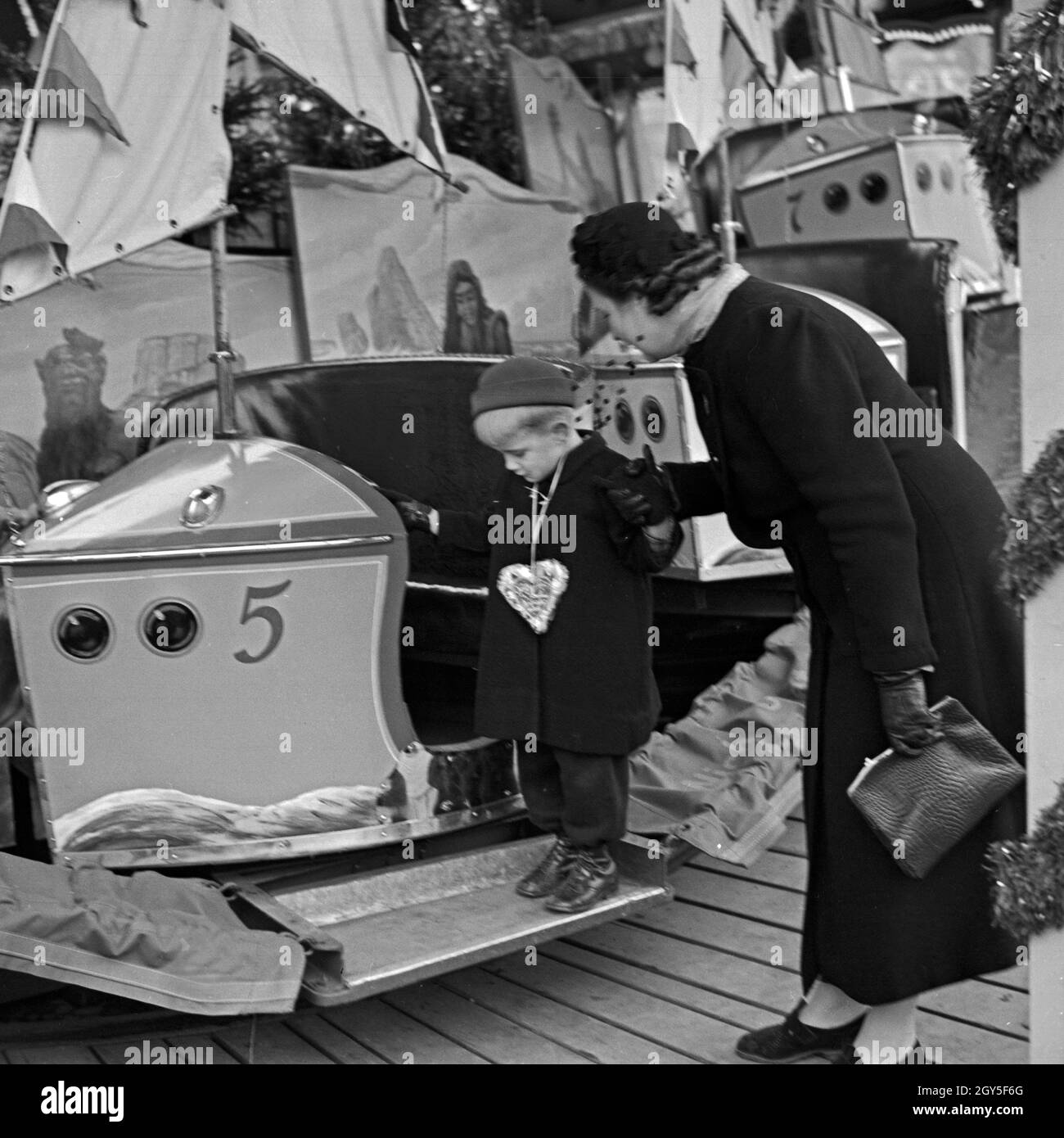 Ein kleiner Junge steht mit circuizione Mutter am Kinderkarussell auf dem Weihnachtsmarkt, Deutschland 1930er Jahre. Un ragazzino e sua madre in piedi da una giostra kiddy presso il mercato di natale, Germania 1930s. Foto Stock