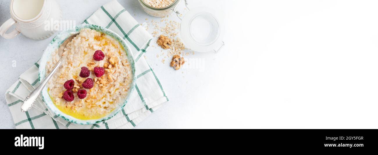 Porridge di farina d'avena con lamponi freschi, noci e burro in un piatto di ceramica su un fondo di pietra leggera o cemento. Messa a fuoco selettiva. Foto Stock