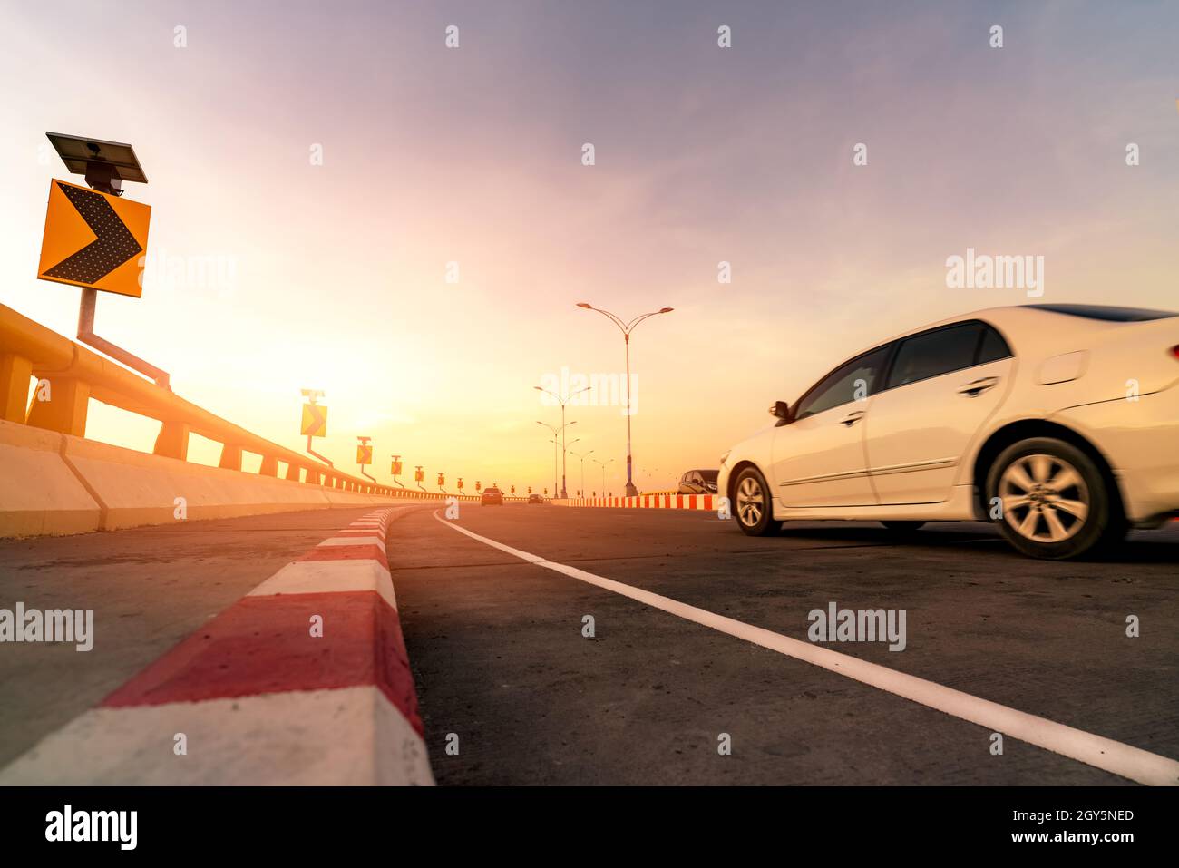 Sfocatura del movimento della macchina bianca che guida su strada in cemento curva con segnale stradale. Viaggio su strada durante le vacanze estive. Auto guidare sulla strada. Viaggio estivo in auto Foto Stock
