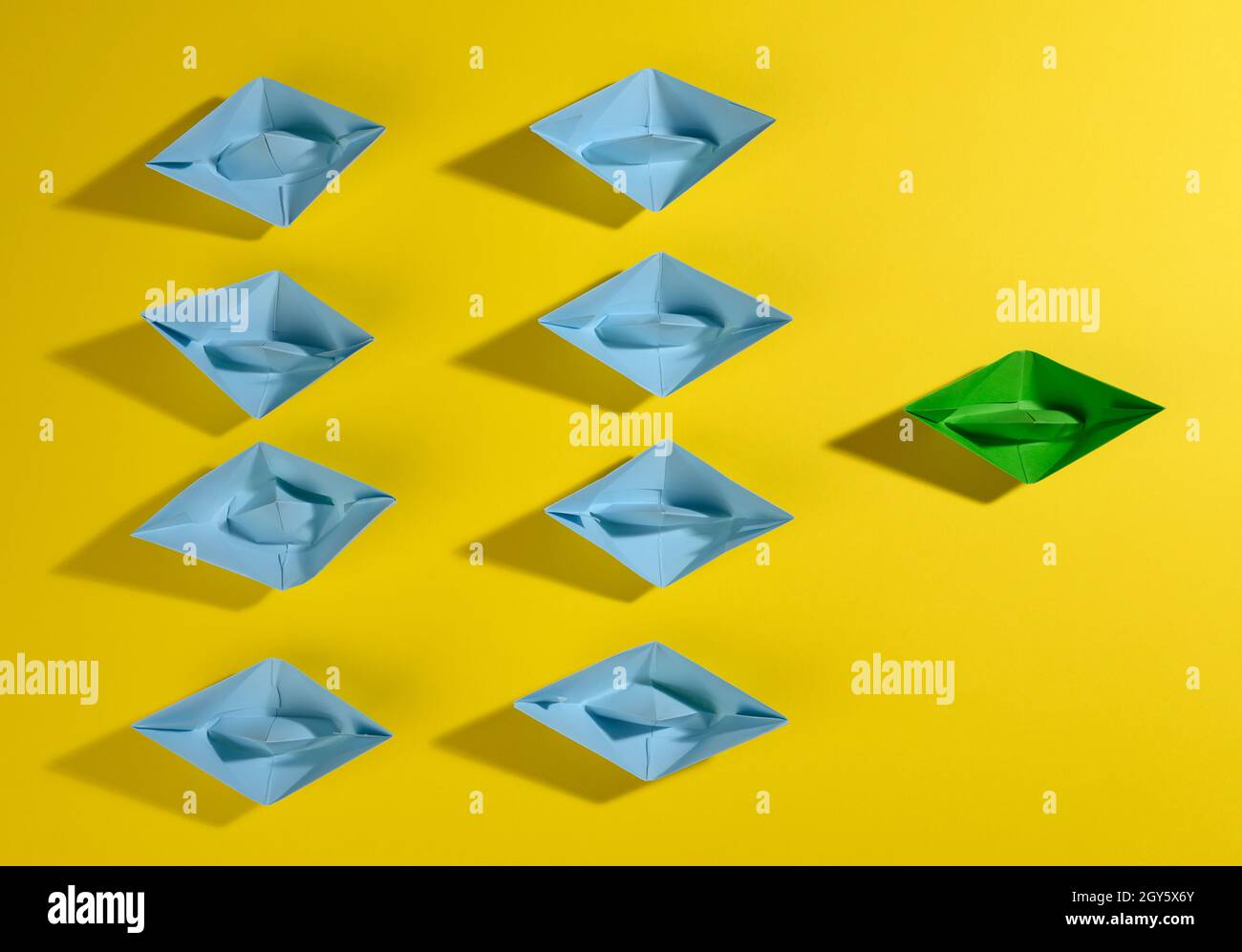 un gruppo di barche di carta blu e una verde led su uno sfondo giallo. Il concetto di un leader forte, la manipolazione delle masse, un team stretto e un Foto Stock