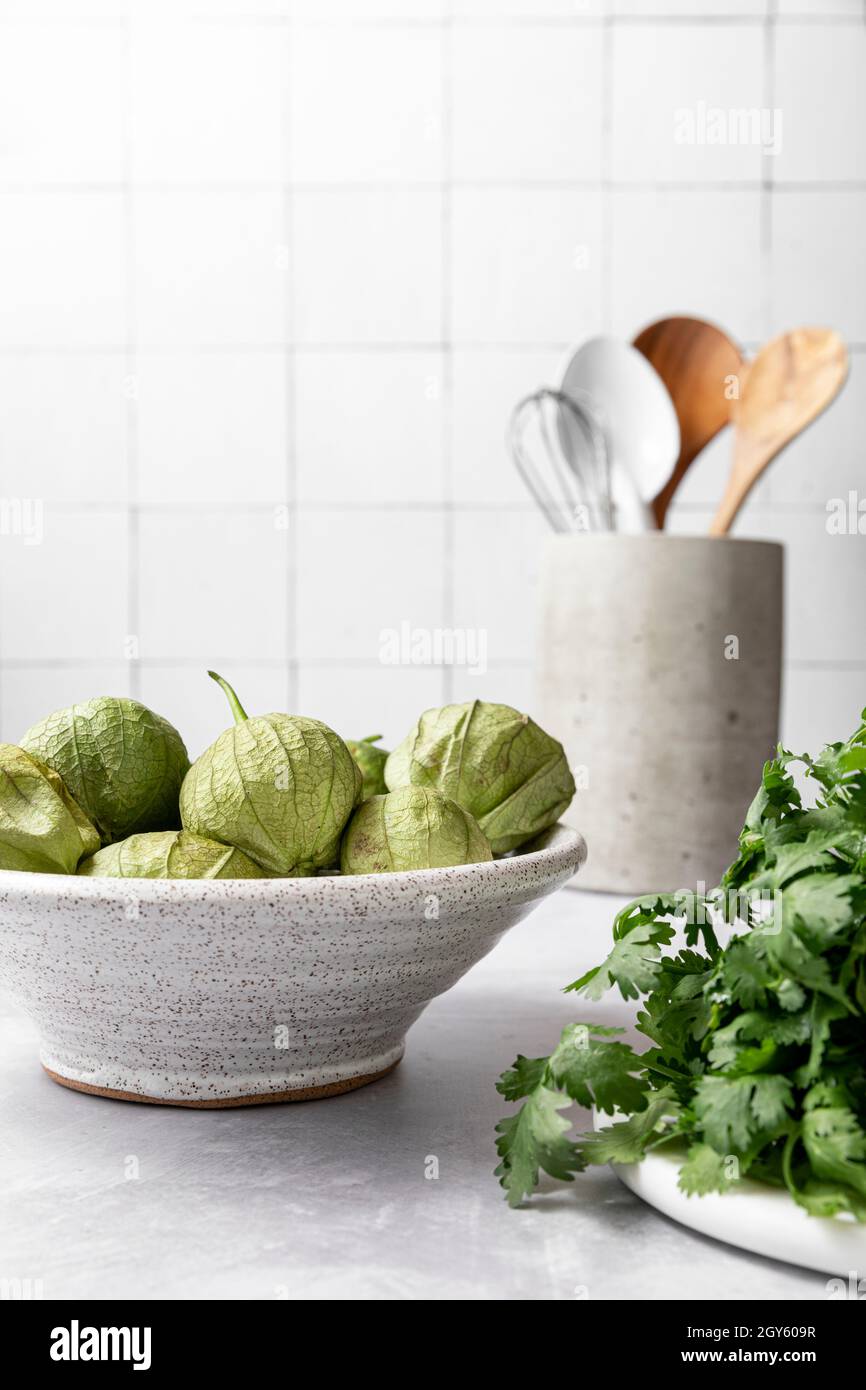 Coriandolo e una ciotola in ceramica piena di tomatillos seduti su un luminoso bancone Foto Stock
