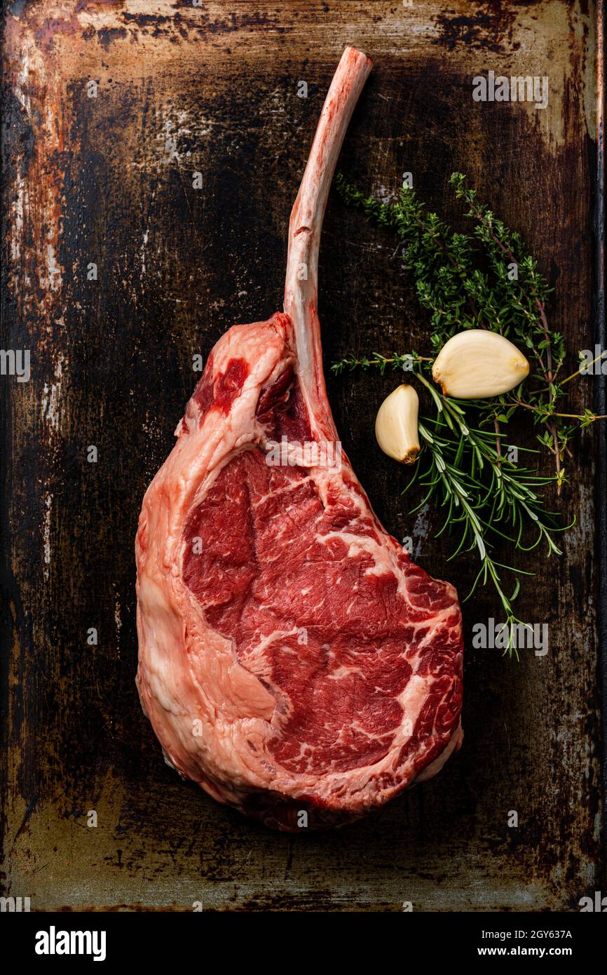 Carne fresca cruda Tomatahawk Steak e condimenti su sfondo scuro foglio da forno Foto Stock