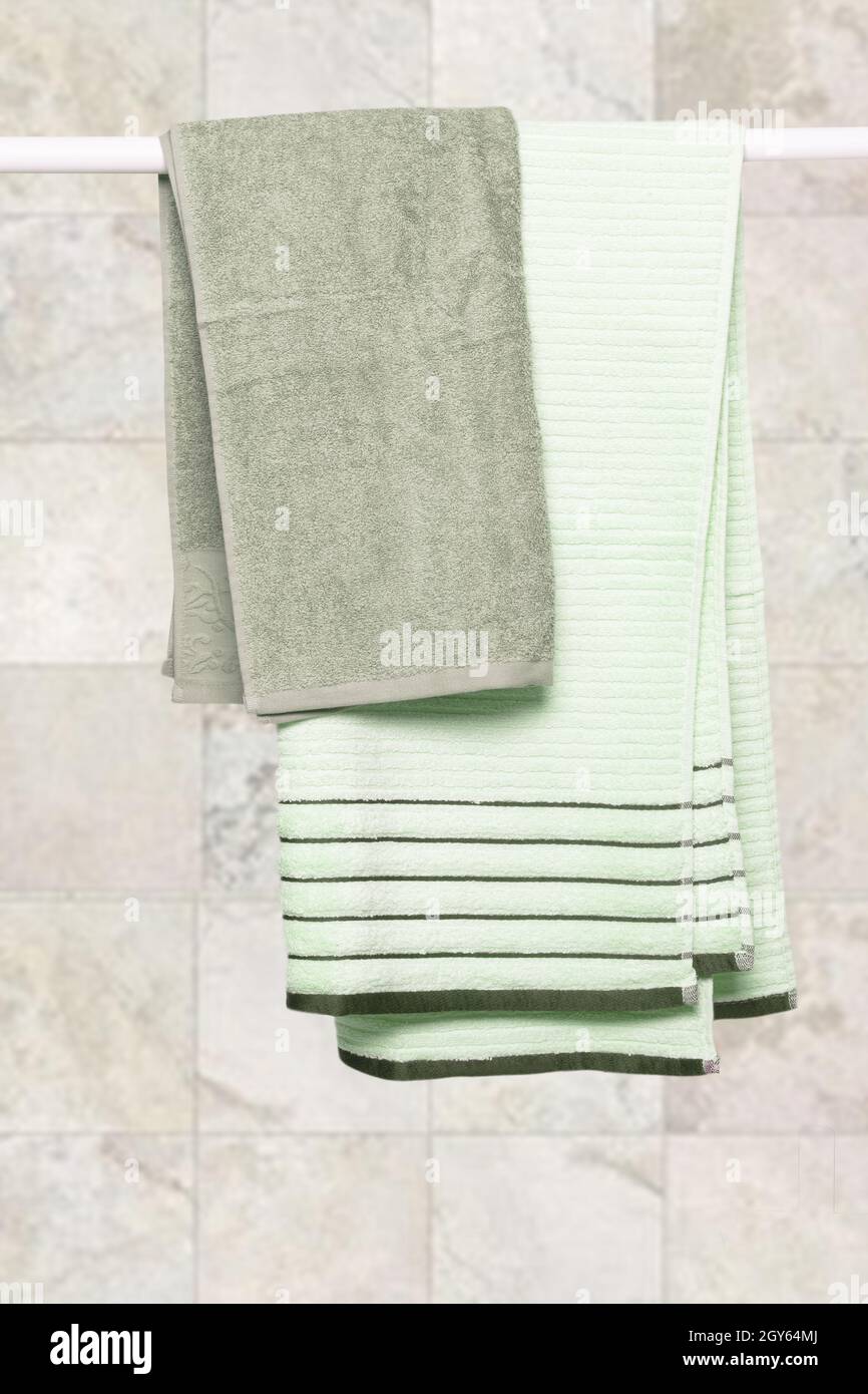Asciugamani appesi. Primo piano di morbidi asciugamani verdi in spugna appesi su un portabiti contro uno sfondo di pietra chiaro e sfocato. Foto Stock