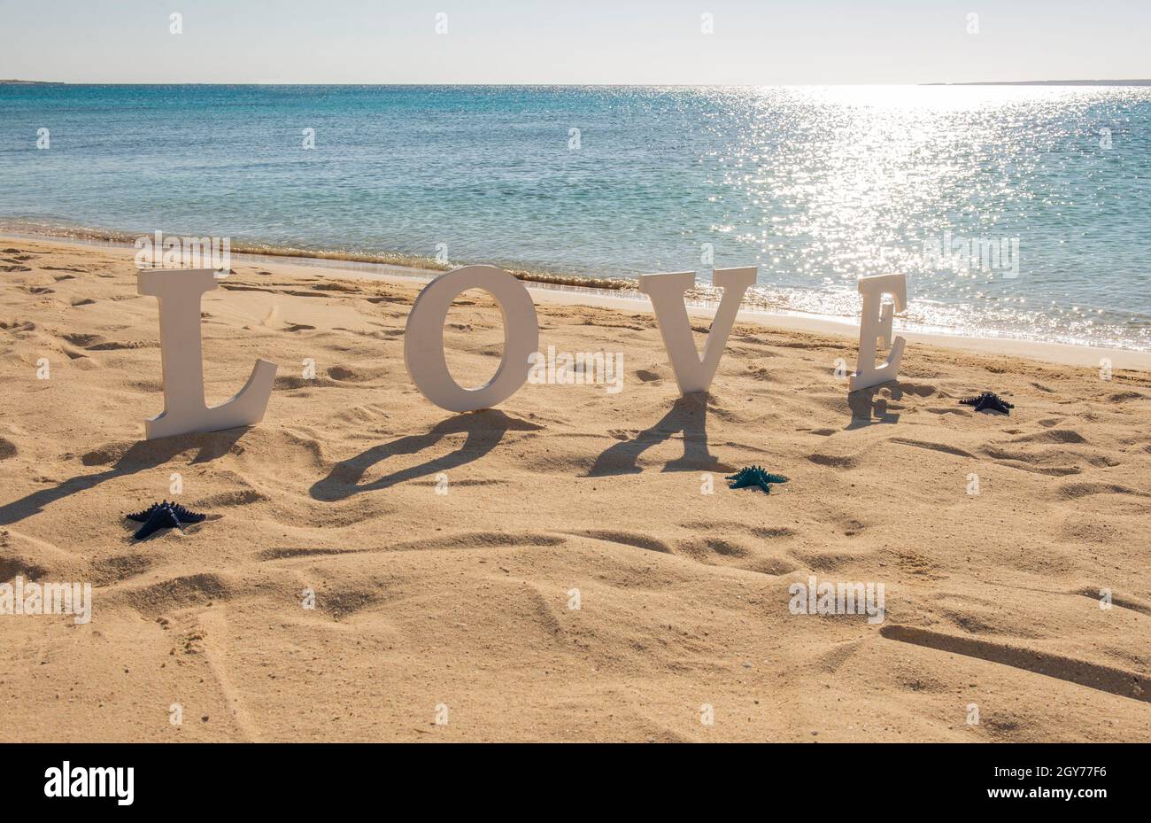 Primo piano di romantico segno d'amore sulla spiaggia di sabbia dell'isola tropicale paradiso con l'oceano sullo sfondo Foto Stock