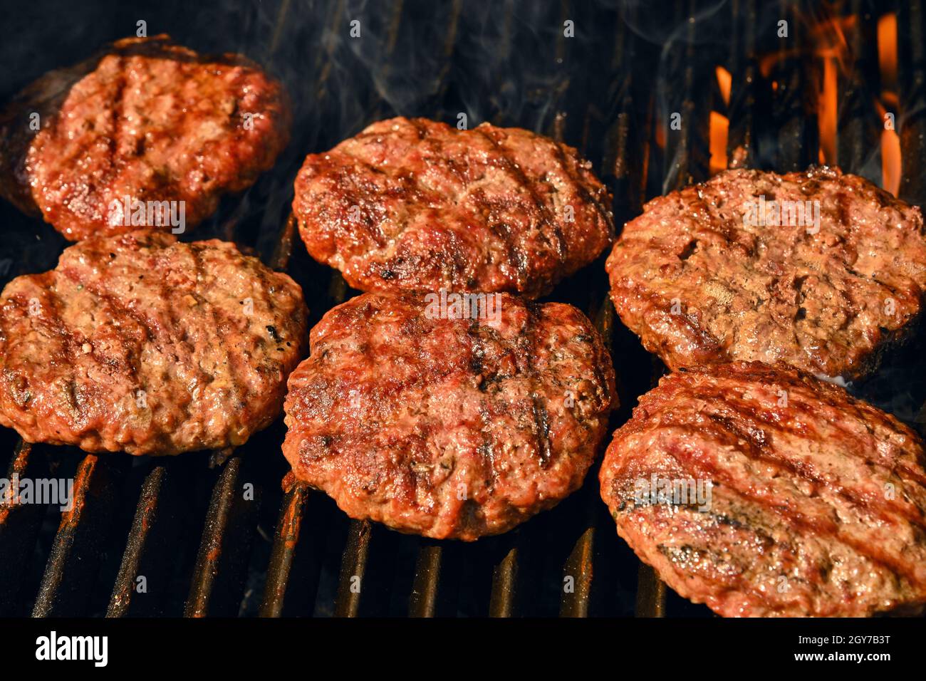 Primo piano di ricerca e fumo manzo o carne di maiale barbecue hamburger per hamburger su barbecue fuoco griglia con griglia in ghisa metallo, vista ad alto angolo Foto Stock