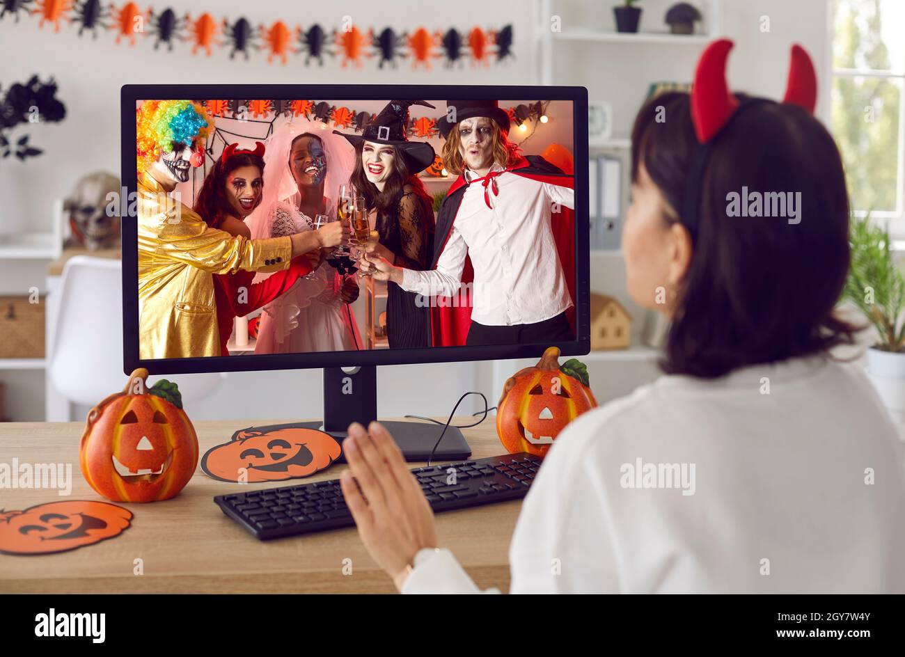 Donna che sventola lo schermo del computer durante una festa virtuale in costume di Halloween con gli amici Foto Stock